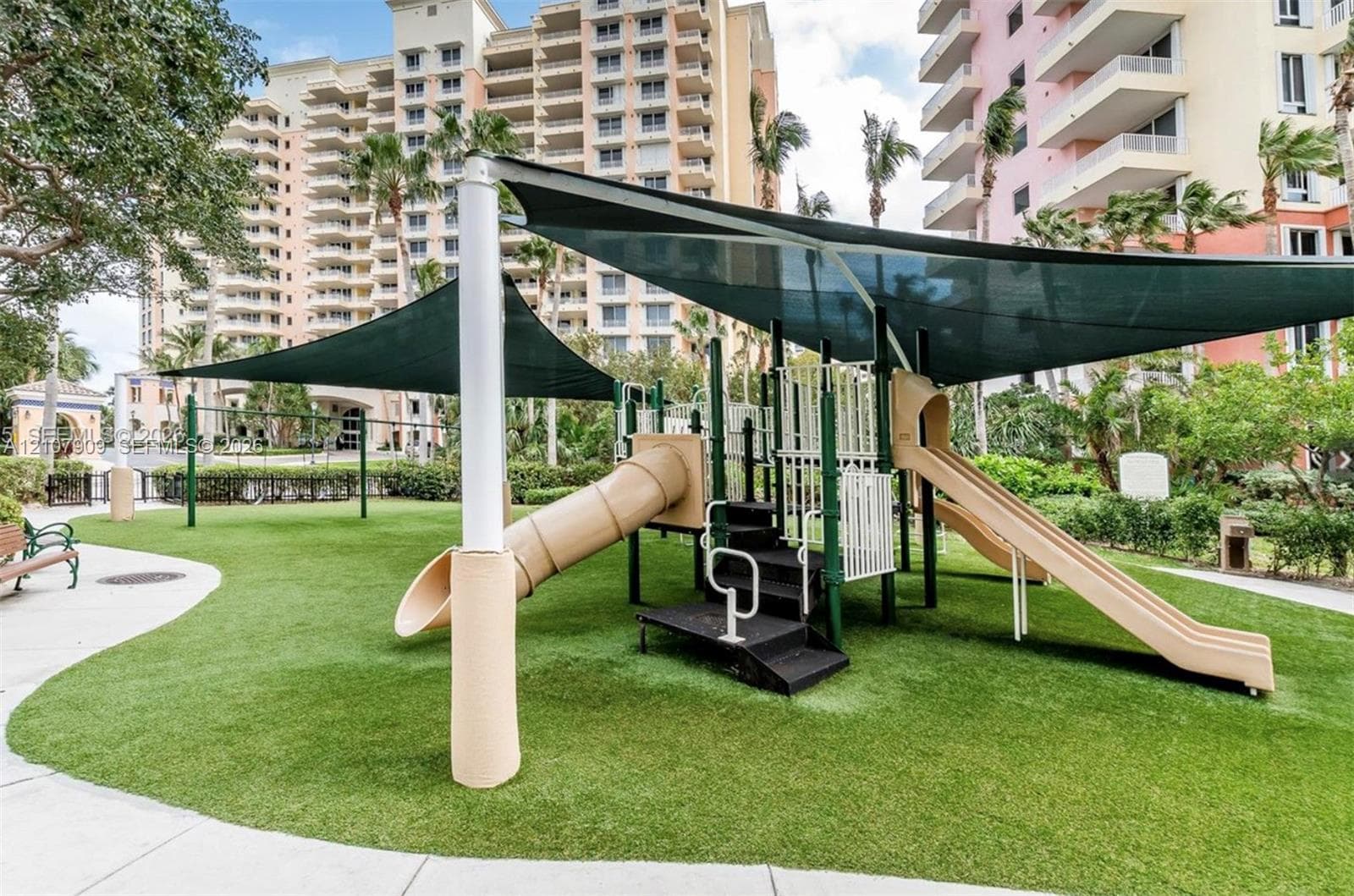 Outdoor recreation area featuring a synthetic turf ground cover, integrated playground structure with dual slides, and overhead shade sails