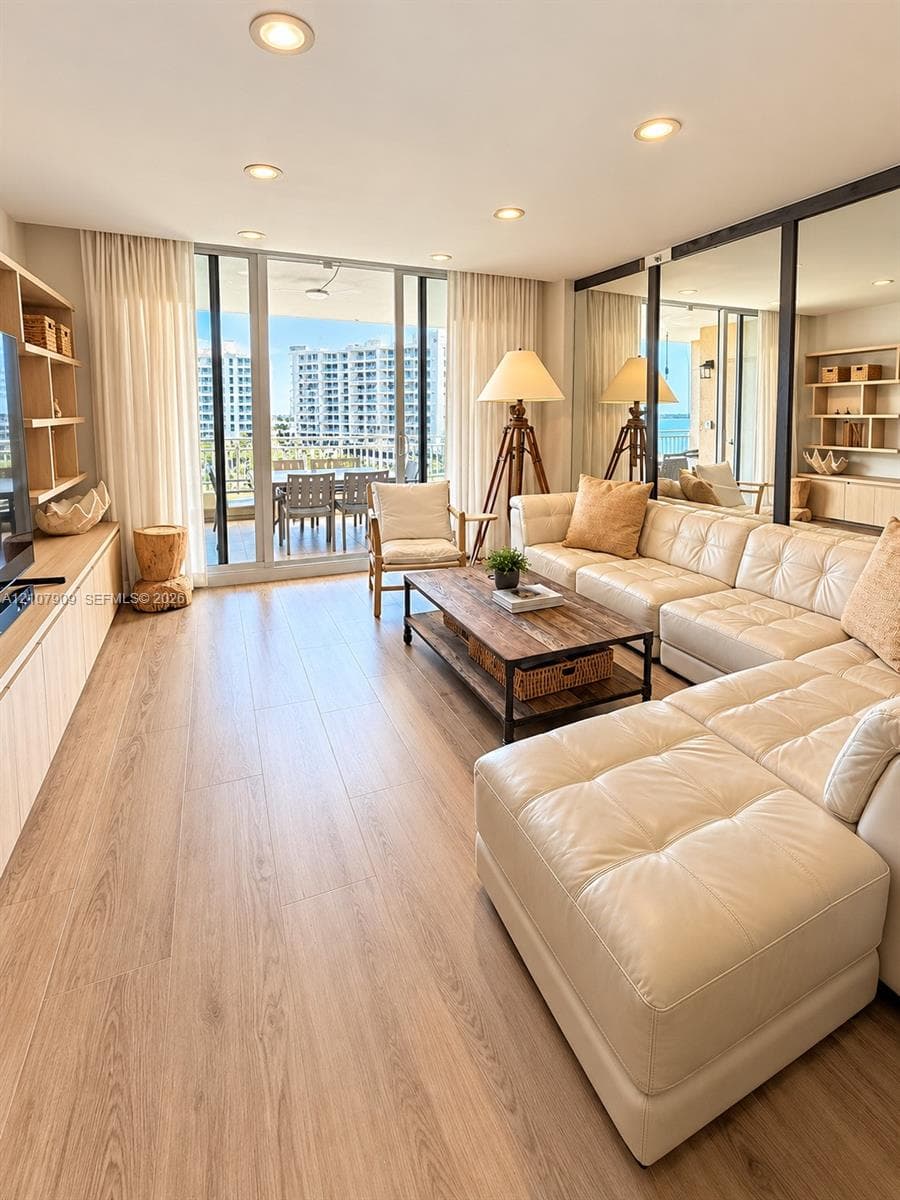 Living area featuring floor-to-ceiling glass sliding doors, wood-finish flooring, built-in light wood cabinetry, recessed lighting, and wall-to-wall mirrors