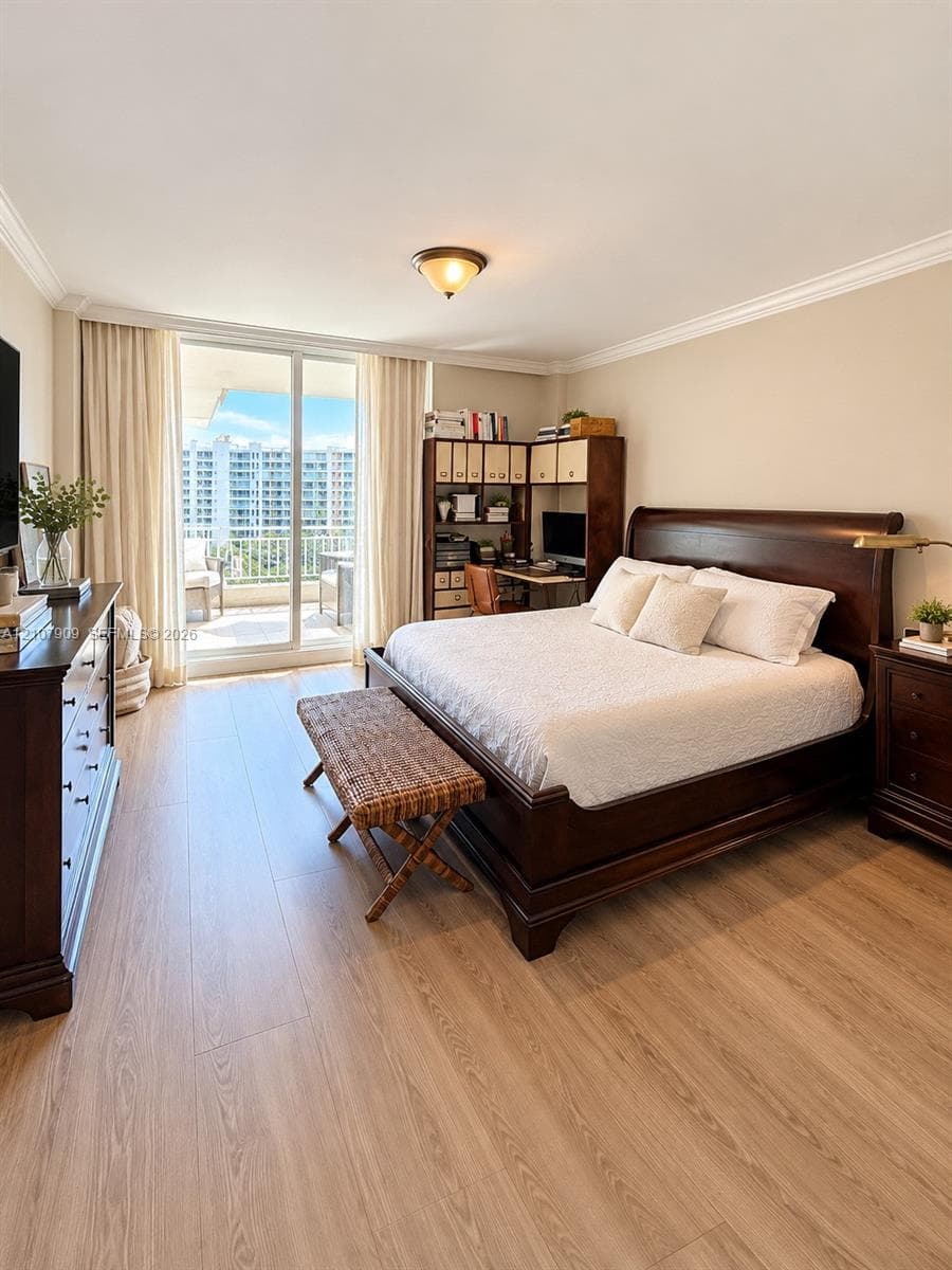Room featuring wood-finish flooring, crown molding, and floor-to-ceiling glass sliding doors opening to a balcony