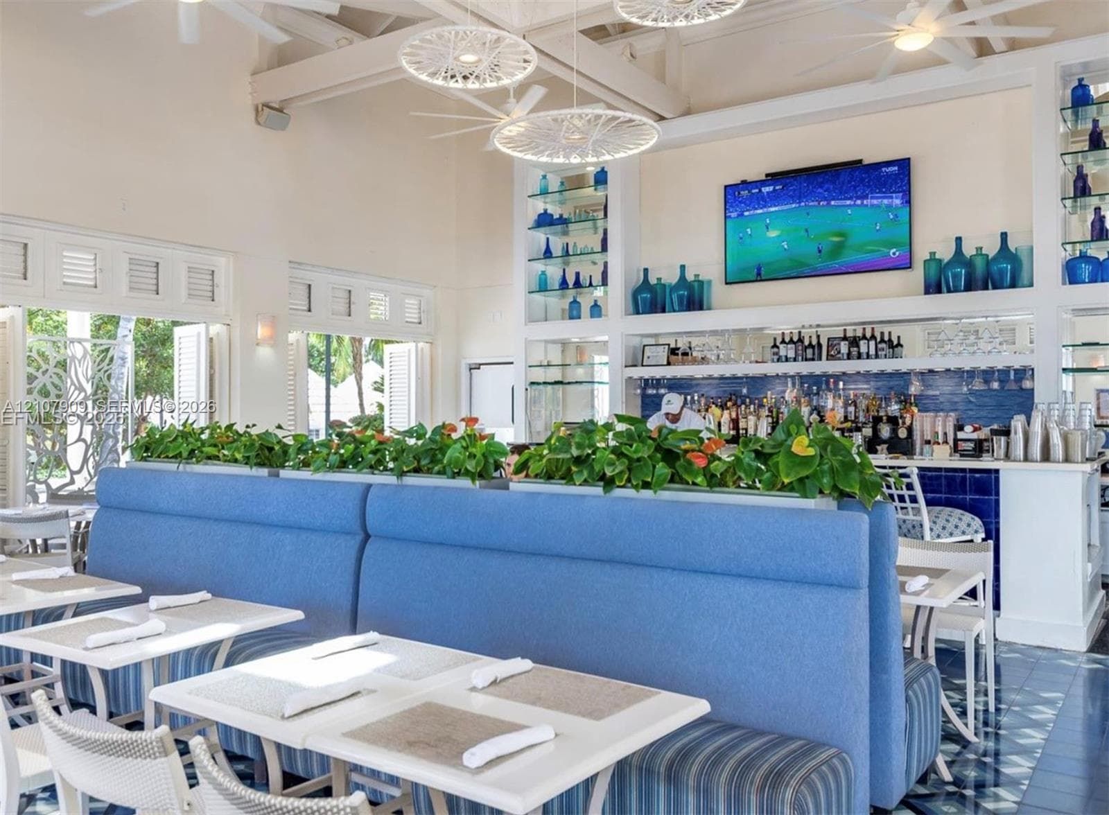 Vaulted ceilings with exposed beams, built-in recessed shelving, decorative pendant lighting, louvered window panels, and integrated bar service area