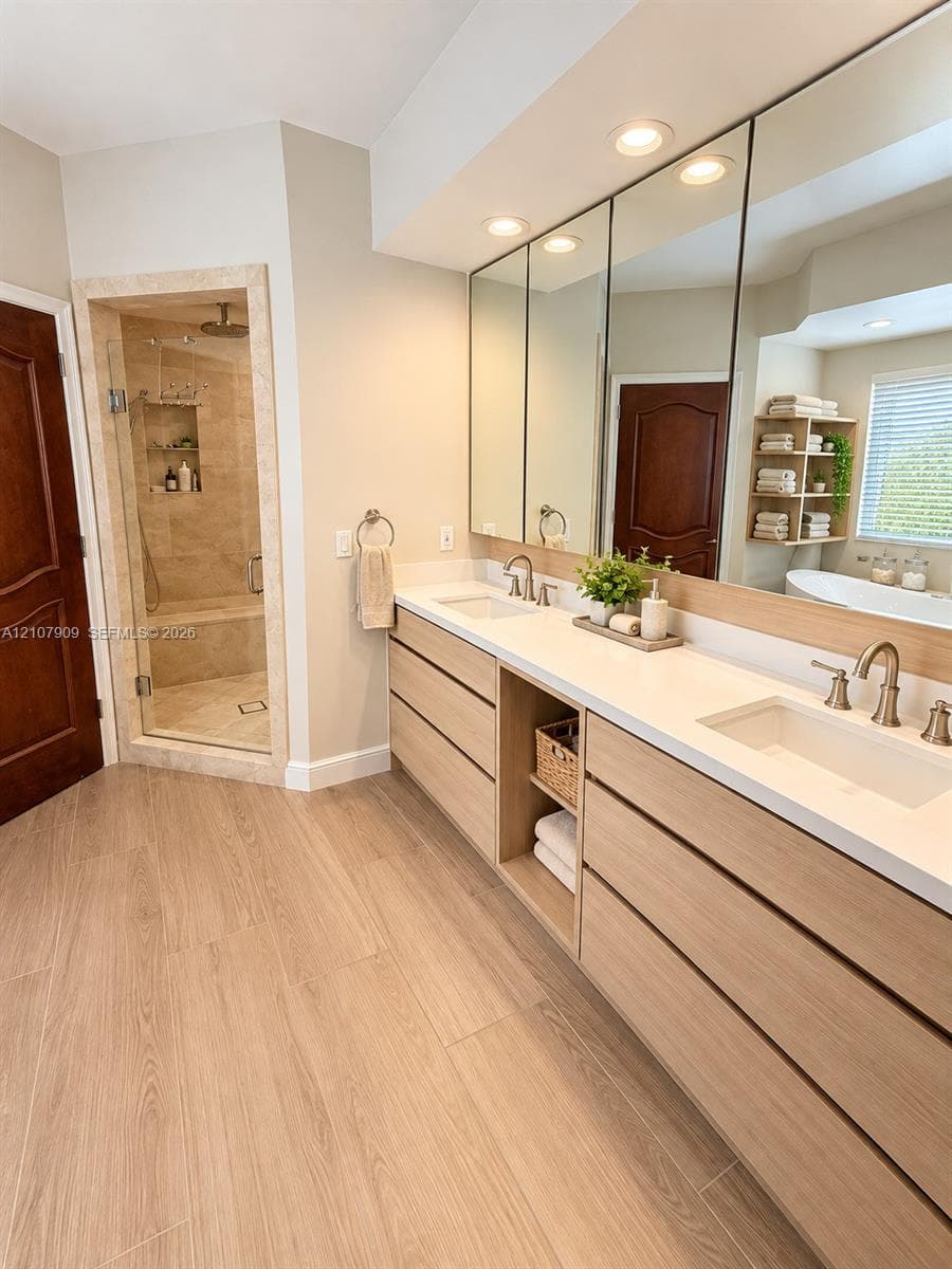 Dual-vanity cabinet featuring light-toned wood cabinetry, stone countertops, integrated under-mount sinks, and widespread faucets, complemented by a walk-in glass-enclosed shower with tiled interior and built-in stone bench seating