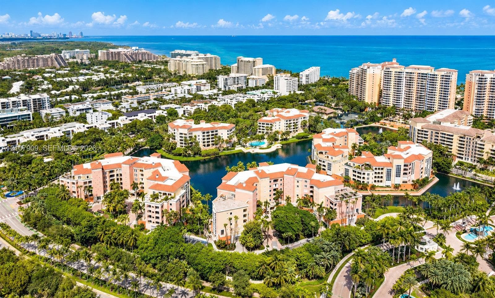 Aerial perspective of coastal residential structures featuring clay-tiled roofs, integrated water features, mature tropical landscaping, and proximity to the shoreline