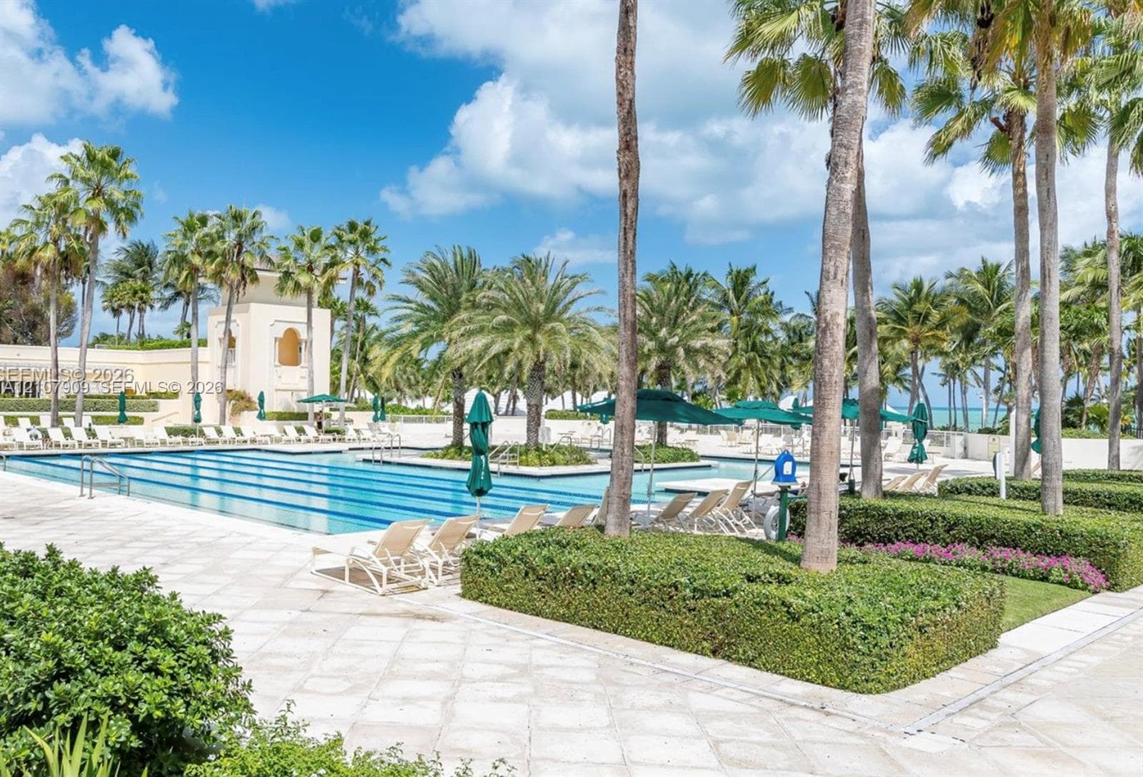 Swimming pool with multi-lane configuration, expansive stone-paver decking, manicured shrubbery, and mature palm trees