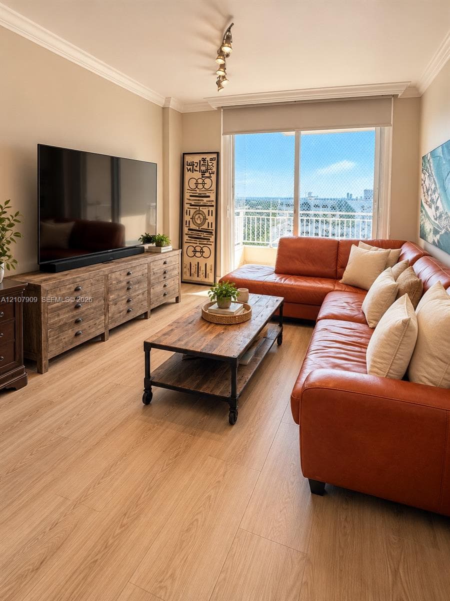Living area featuring wood-finish flooring, crown molding, track lighting, and a large sliding glass door with access to an exterior balcony