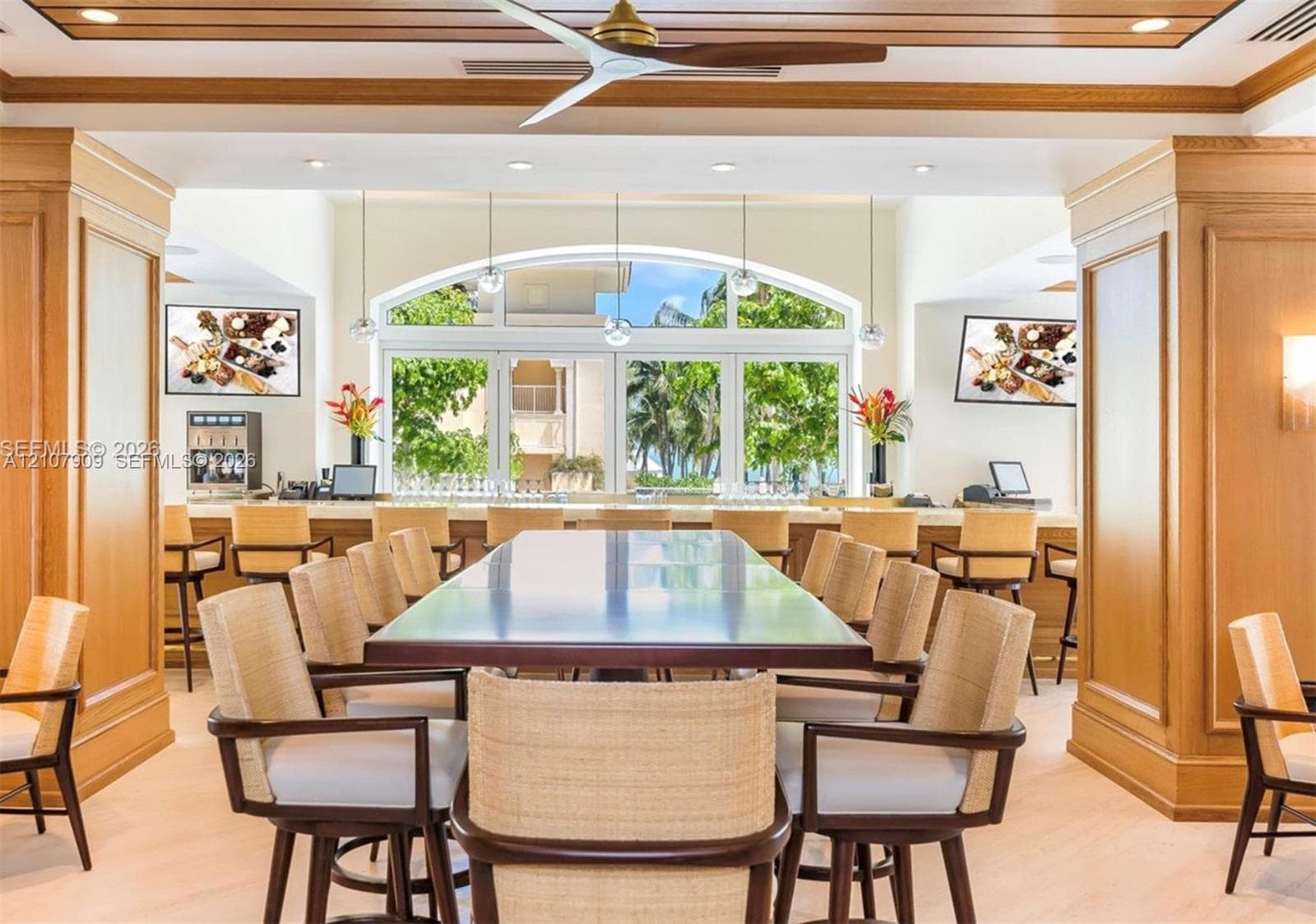 Custom wood-paneled walls and ceiling, large arched window, built-in service bar with stone countertop, ceiling fan with wood-finish blades, and recessed lighting