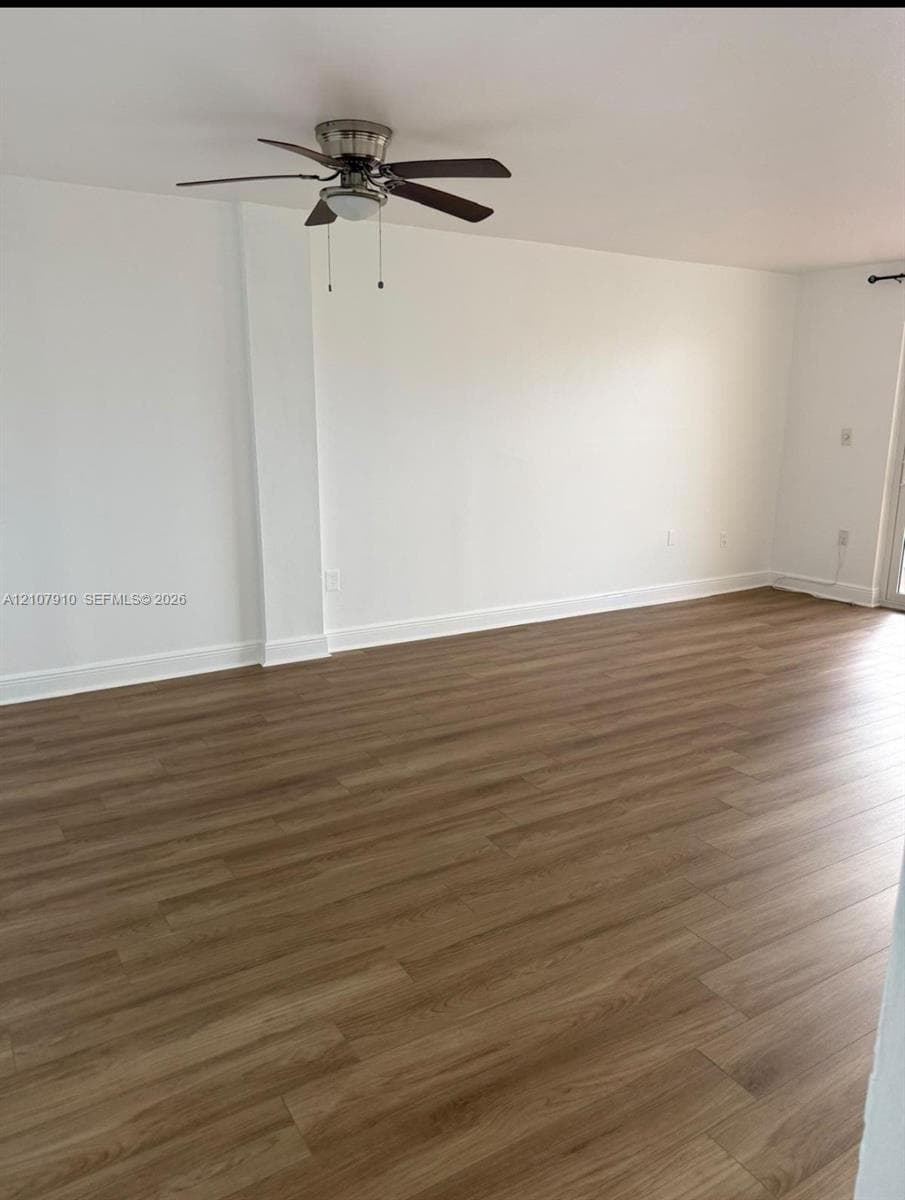 Interior space featuring wood-finish flooring, white walls, and a ceiling-mounted light fixture with a multi-blade fan