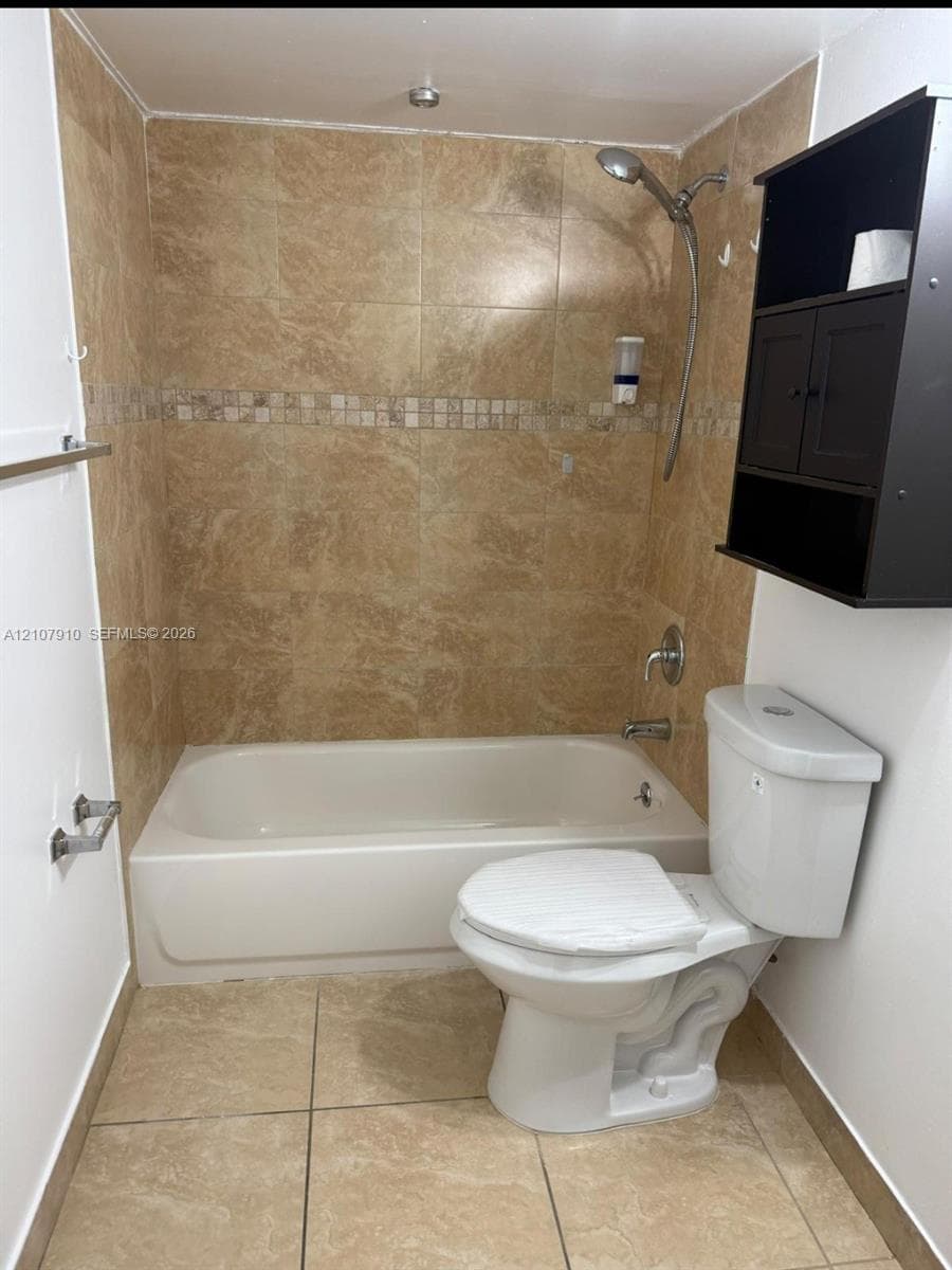 Full-size bathtub with integrated shower, stone-pattern tile surround with decorative mosaic accent strip, and large-format tile flooring