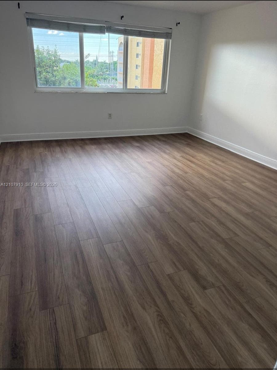 Room interior featuring wood-finish flooring, neutral wall tones, and a large window with roller shades