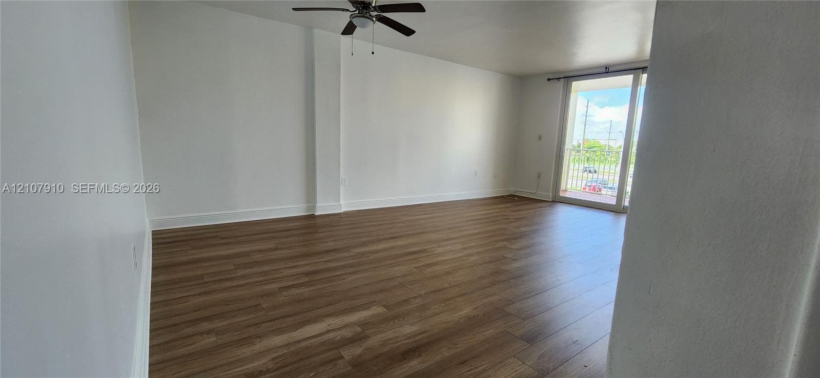 Open-concept living space featuring wood-finish flooring, white walls, a ceiling fan, and sliding glass doors to a balcony