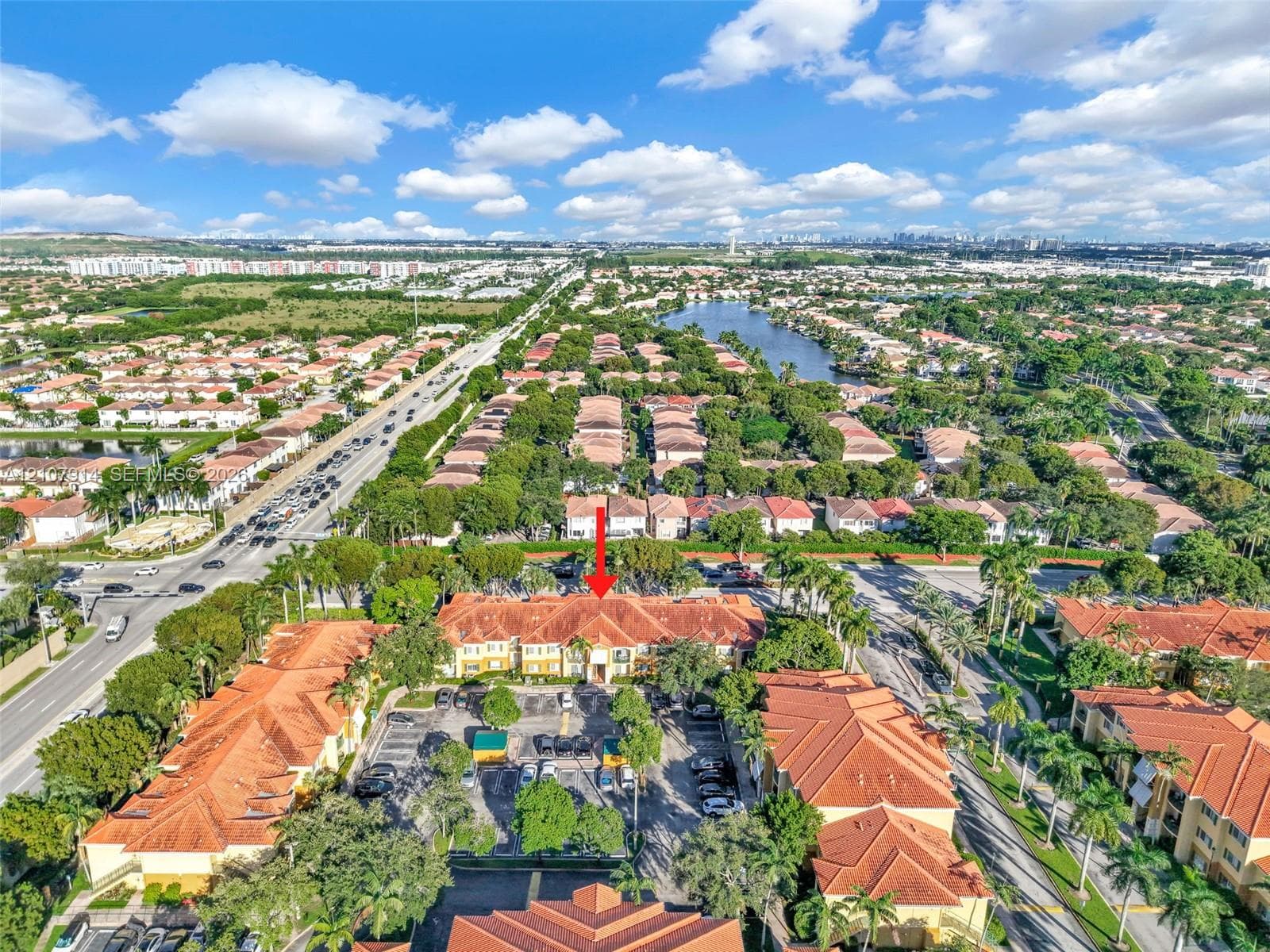 Aerial perspective of a multi-story residential building featuring terracotta tile roofing, stucco exterior, and a dedicated surface parking area surrounded by palm trees and mature landscaping