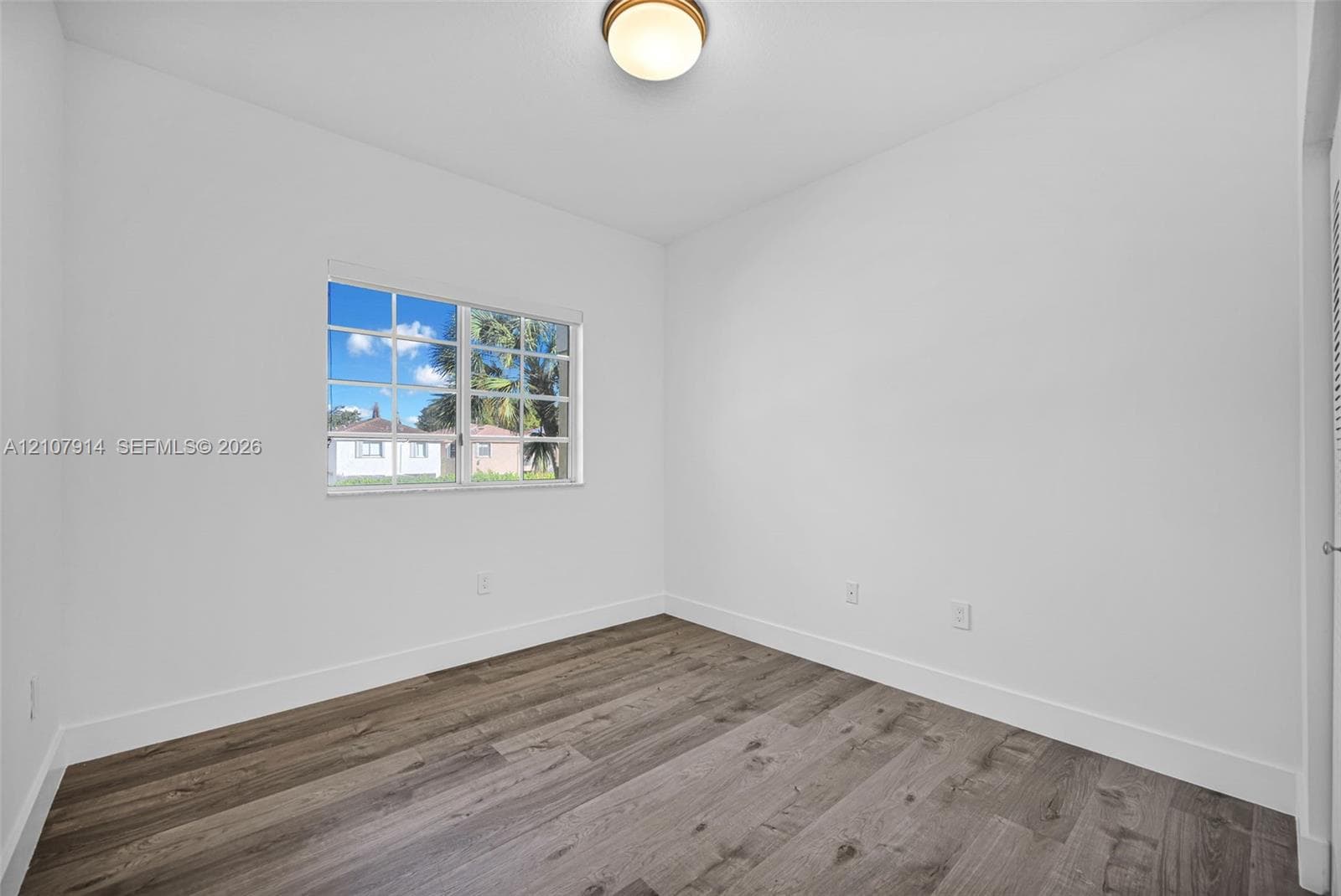 Interior room featuring wood-finish flooring, a multi-pane window, and a central flush-mount ceiling fixture