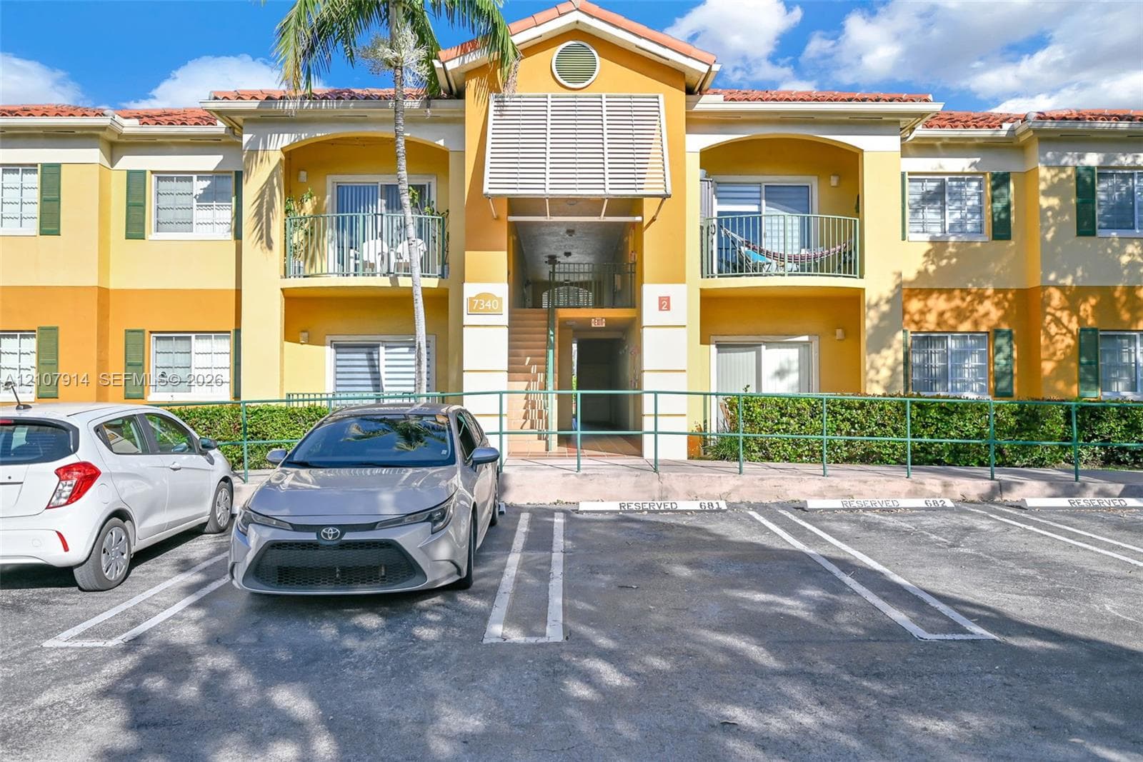 Exterior facade featuring a tile roof, stucco finish, shuttered windows, and private balconies with metal railings