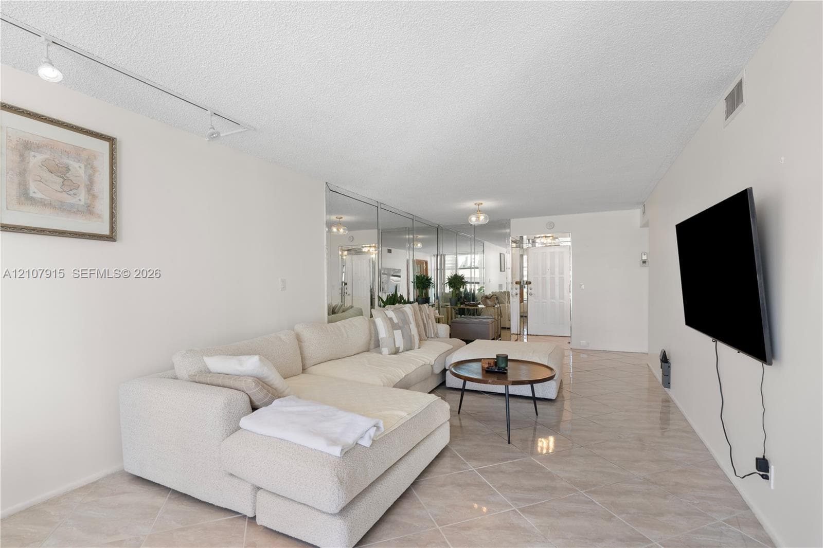 Neutral-toned interior space featuring diagonal-patterned ceramic tile flooring, full-wall mirrored paneling, and adjustable track lighting