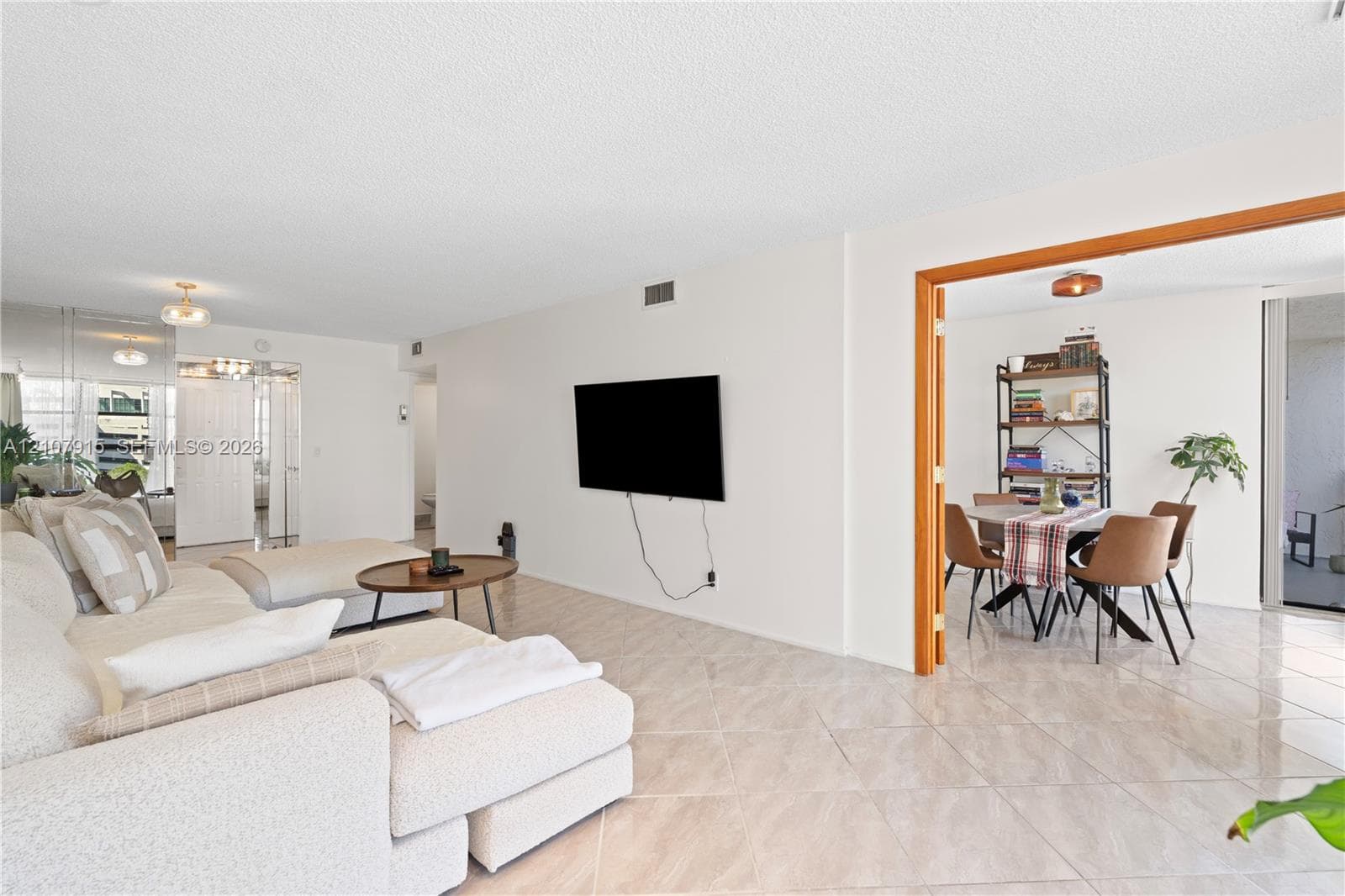 Open-concept interior featuring light-toned tile flooring, neutral wall finishes, and a wide interior doorway framed with wood trim