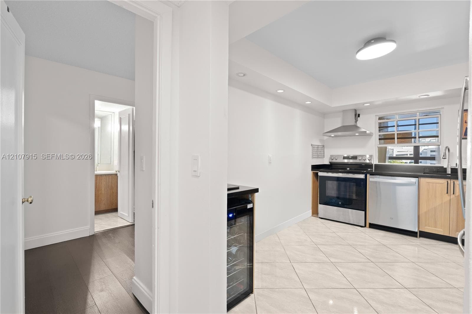 Kitchen featuring stainless steel appliances, light wood cabinetry, stone countertops, a built-in wine refrigerator, and tile flooring