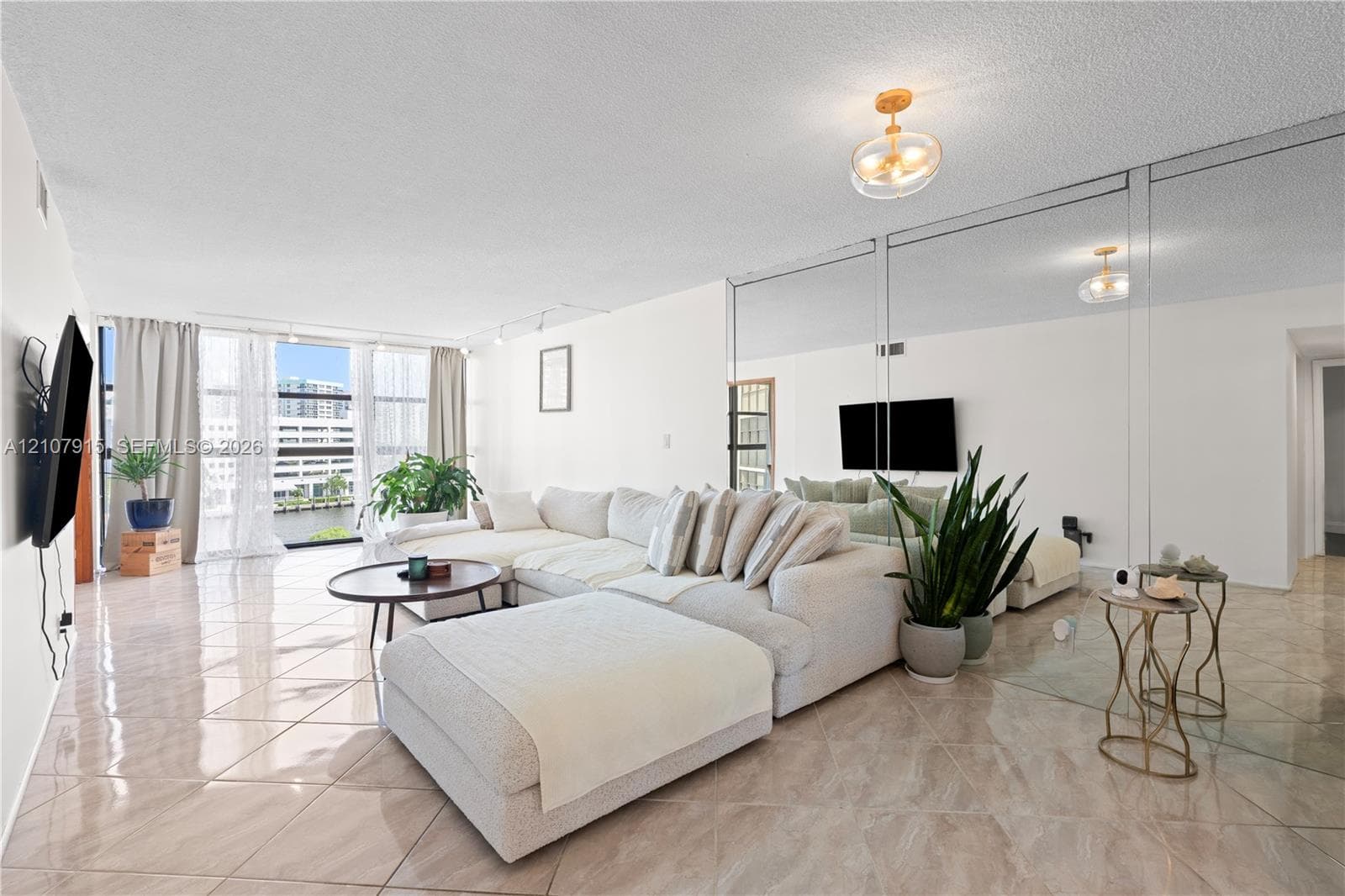 Living area featuring oversized floor-to-ceiling windows, polished tile flooring, full-wall mirrored paneling, and a contemporary flush-mount ceiling light fixture