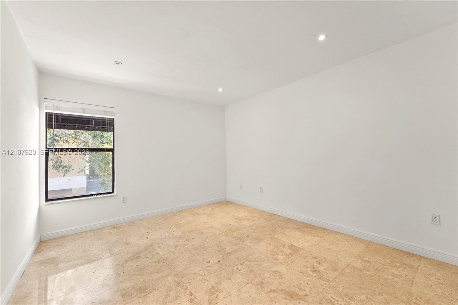 Bright corner room featuring abundant natural light from a large multi-pane window, recessed ceiling lighting, smooth drywall finishes, and light wood-finish flooring throughout