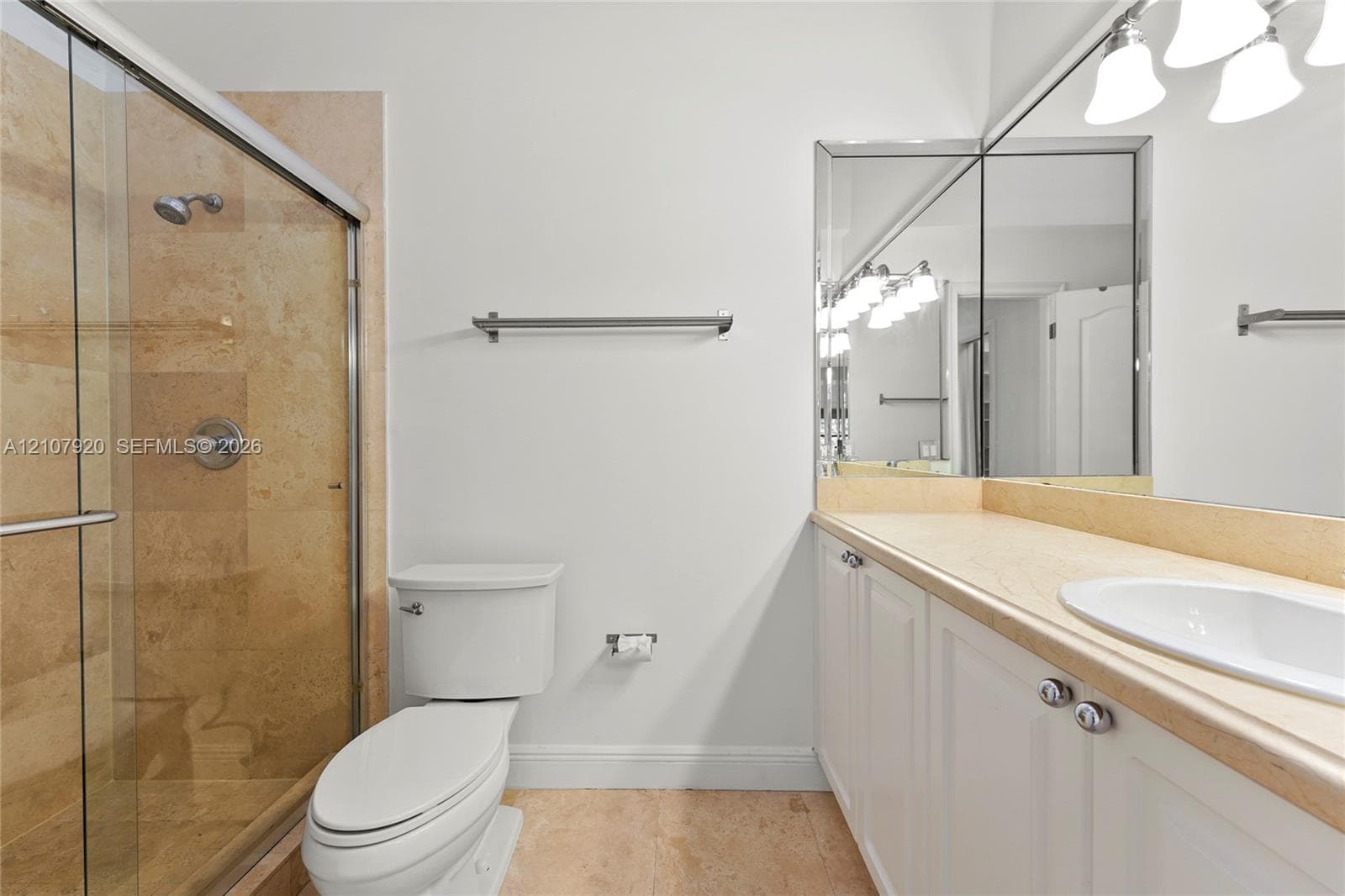 Walk-in shower with stone tile surround, vanity with stone countertop, integrated undermount sink, expansive vanity mirror, and polished metal fixtures