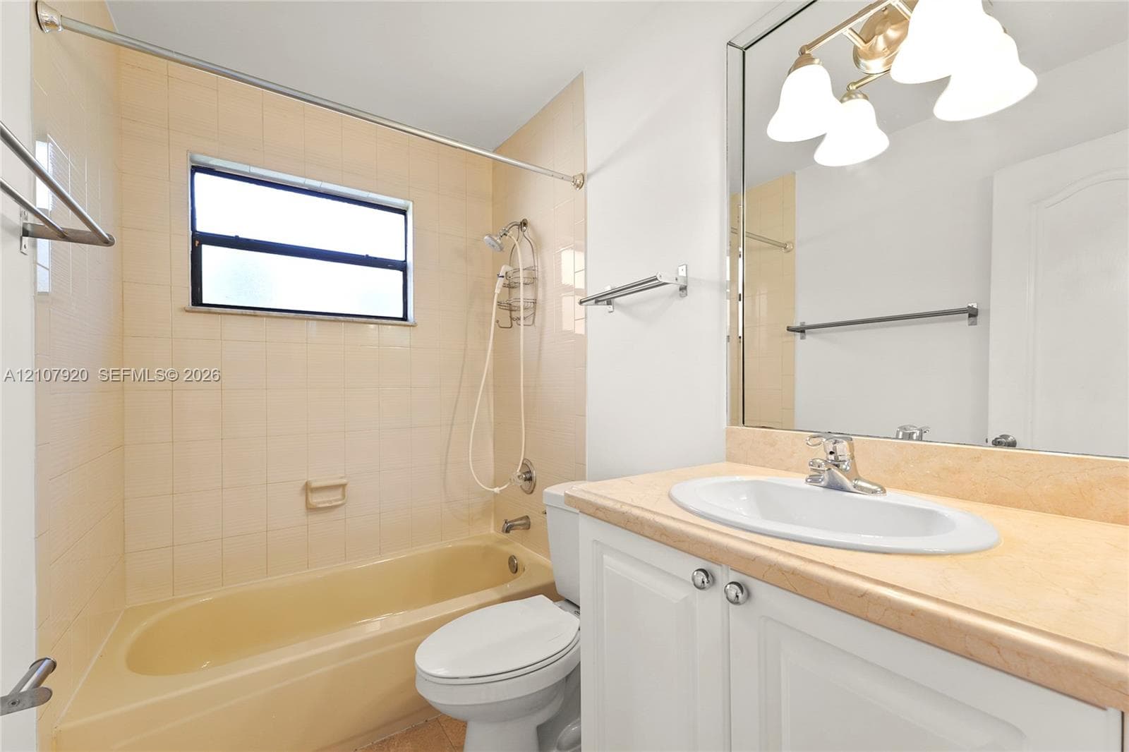 Bathroom featuring a neutral-toned tile shower surround, a built-in tub, a white vanity with a light-colored countertop, and a large-format mirror with integrated three-bulb lighting