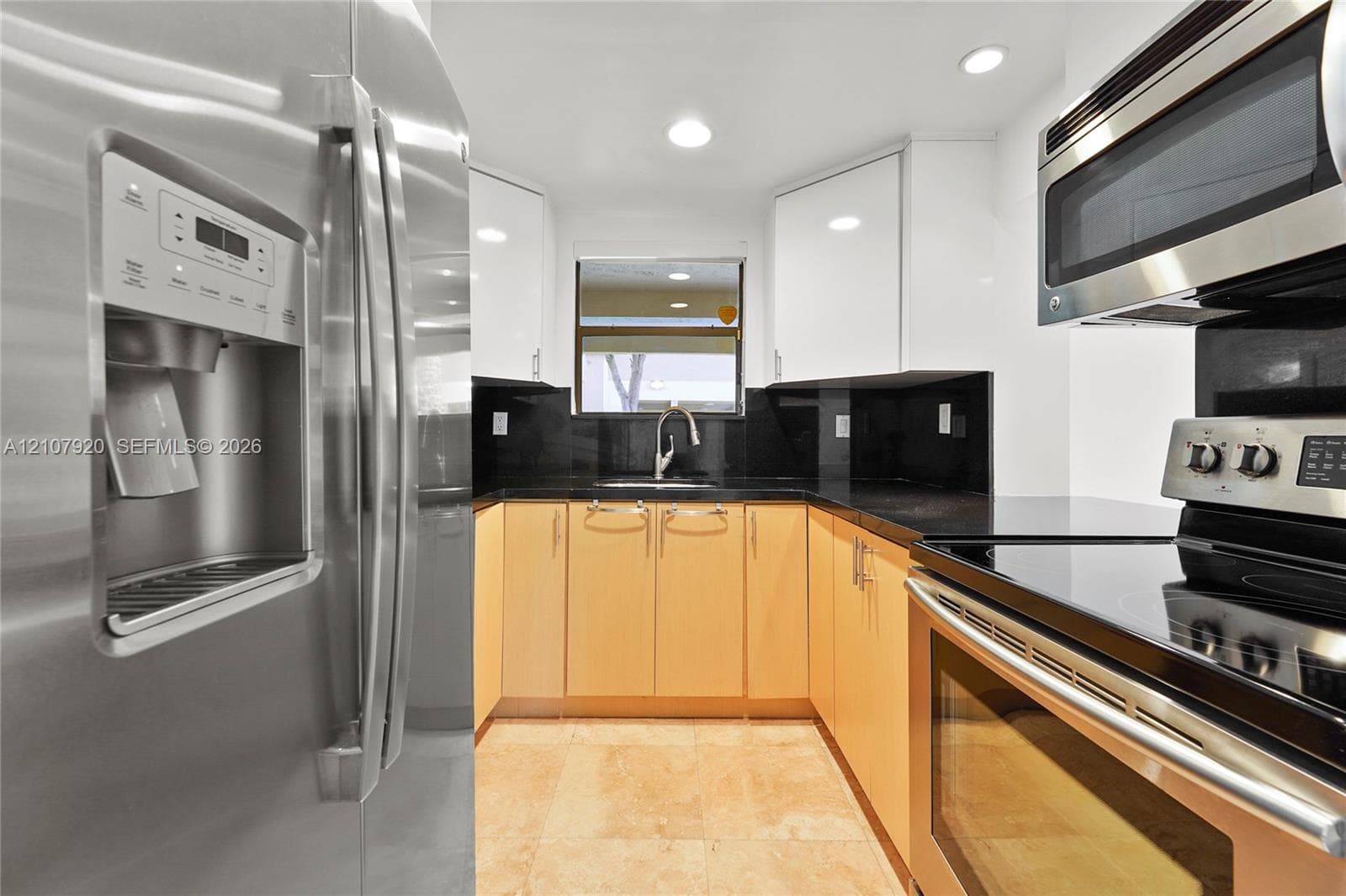 Kitchen featuring stainless steel appliances, dark stone countertops, high-gloss upper cabinetry, wood-finish lower cabinetry, and tile flooring