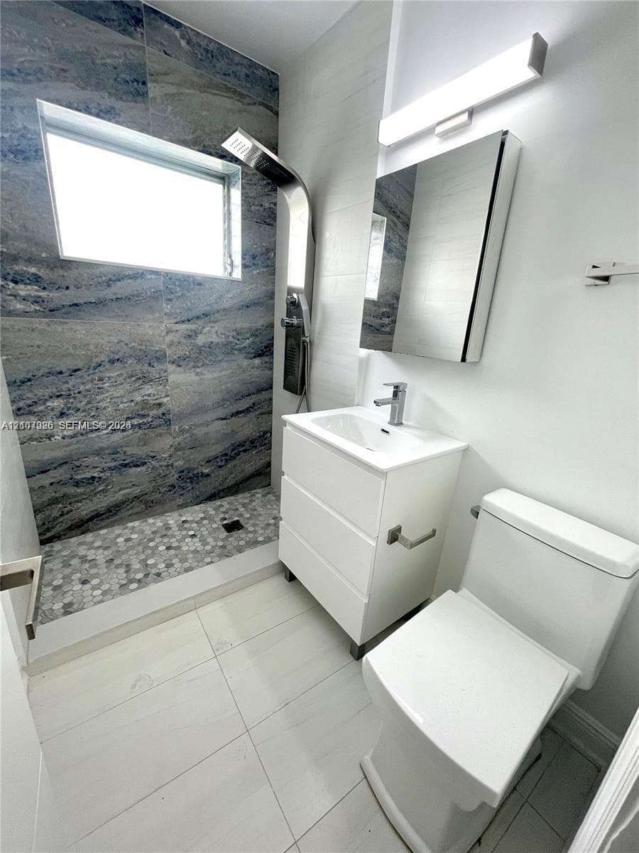 Bathroom featuring a walk-in shower with stone-look wall tiling and a pebble-tiled floor, a wall-mounted shower panel system, a white vanity with an integrated sink, and a mirrored medicine cabinet