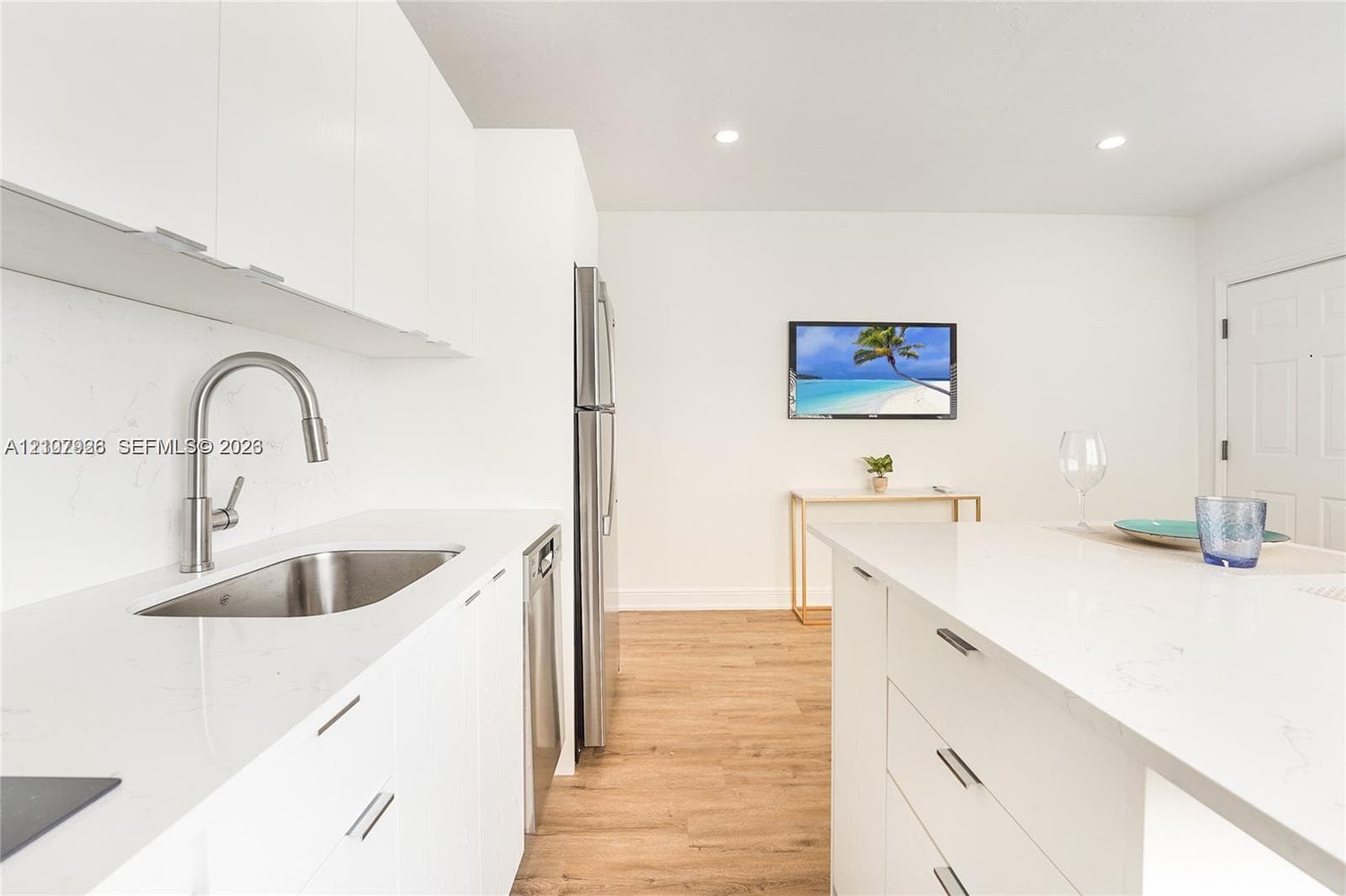 Kitchen featuring white flat-panel cabinetry, a stainless steel undermount sink with a gooseneck faucet, light-toned stone-finish countertops, stainless steel appliances, and wood-finish flooring