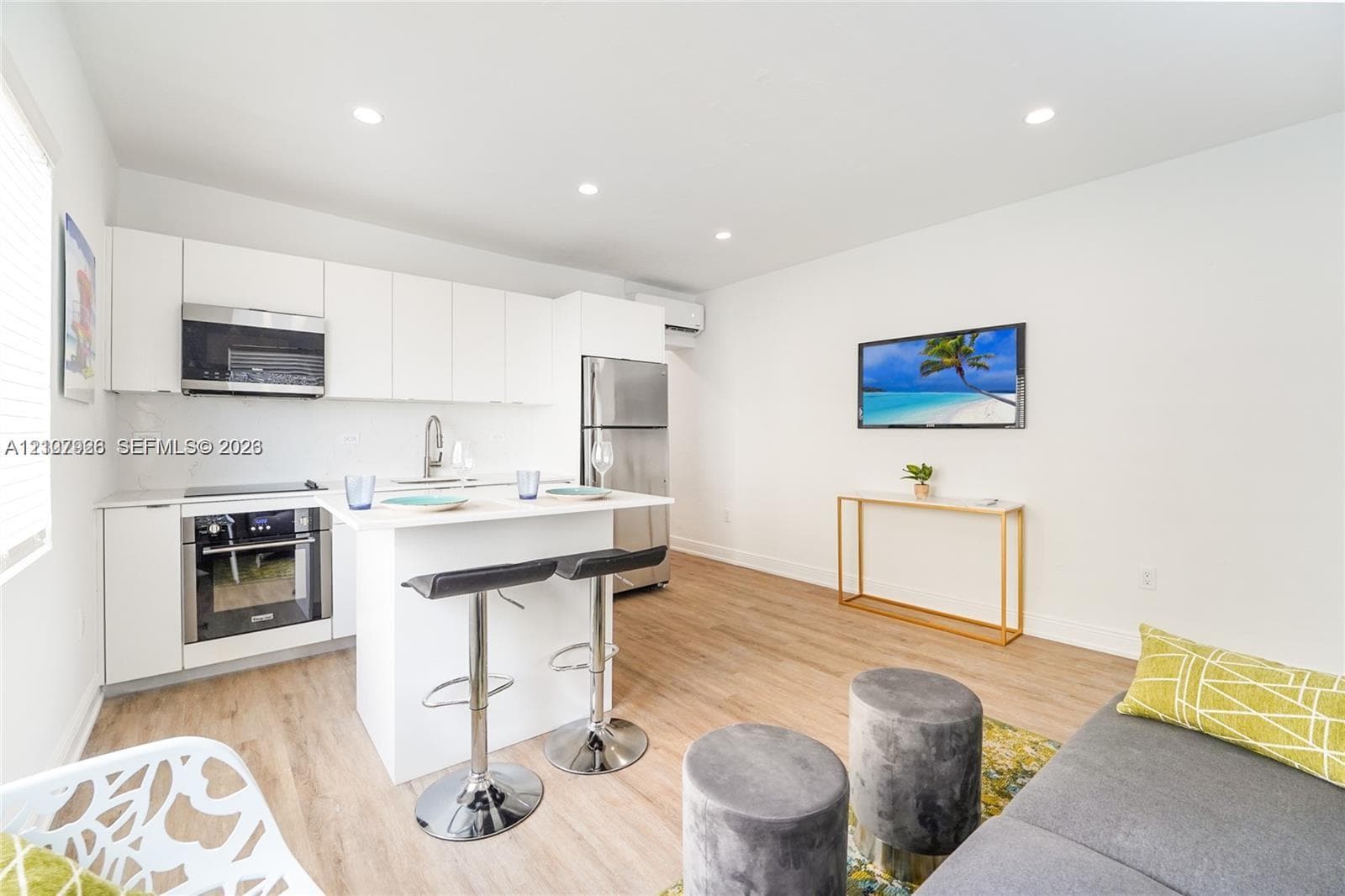 Open-concept kitchen featuring white flat-panel cabinetry, stainless steel appliances, a central island, and wood-finish flooring