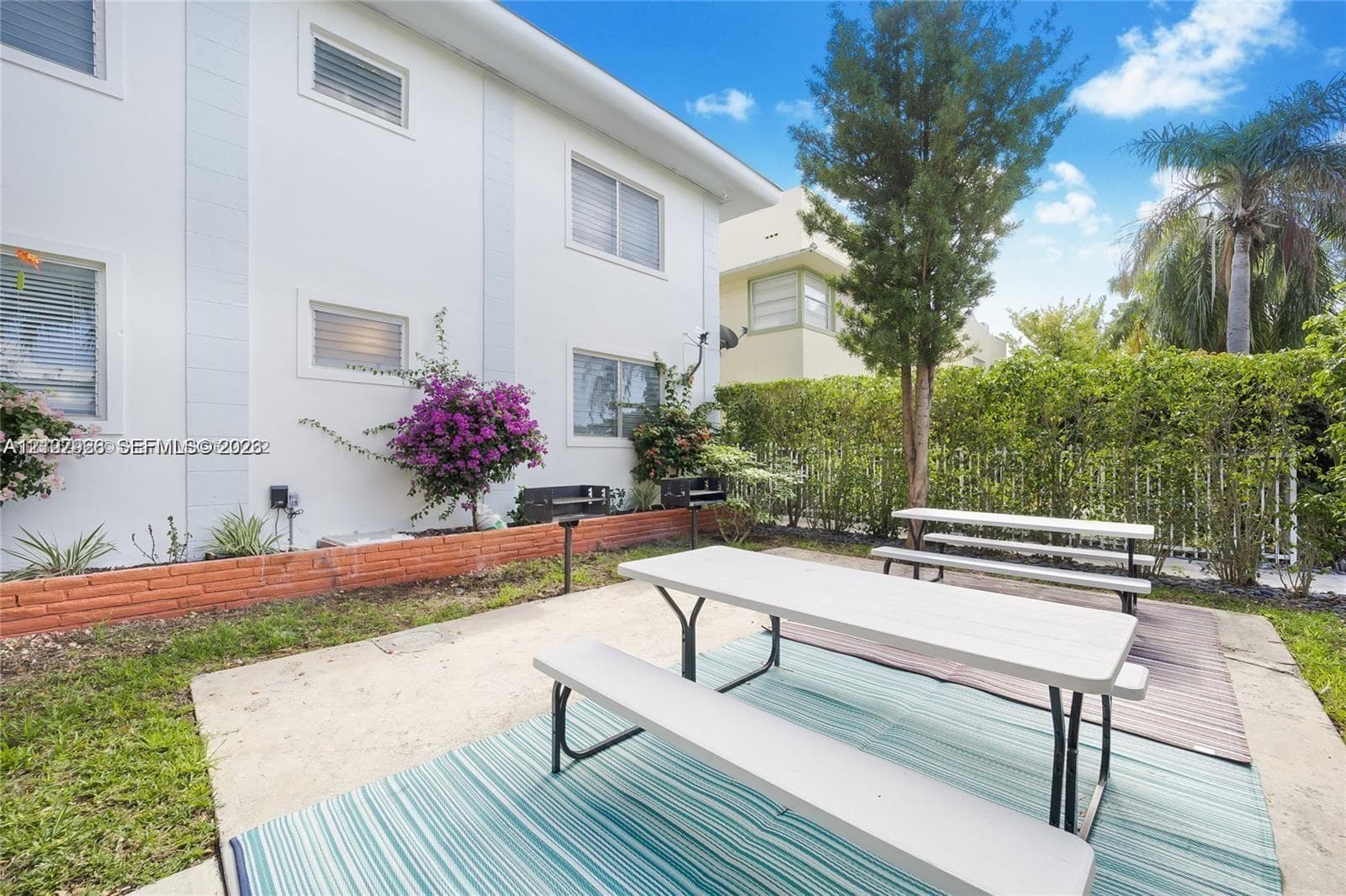 Outdoor recreation area featuring a concrete patio, built-in charcoal grills, low-profile brick retaining wall, and mature landscaping