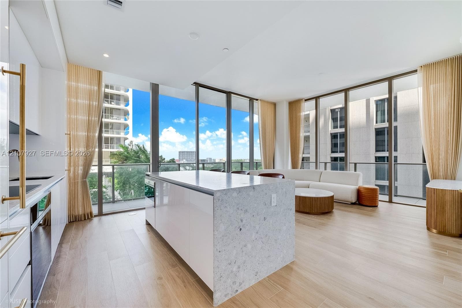 Kitchen featuring a central island with a stone-finish countertop, high-gloss cabinetry, floor-to-ceiling glass windows, and wood-finish flooring