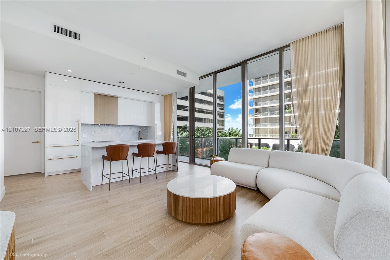 Open-concept living space featuring wood-finish flooring, floor-to-ceiling windows, and a modern kitchen with a stone-top island, gloss-finish cabinetry, and built-in appliances