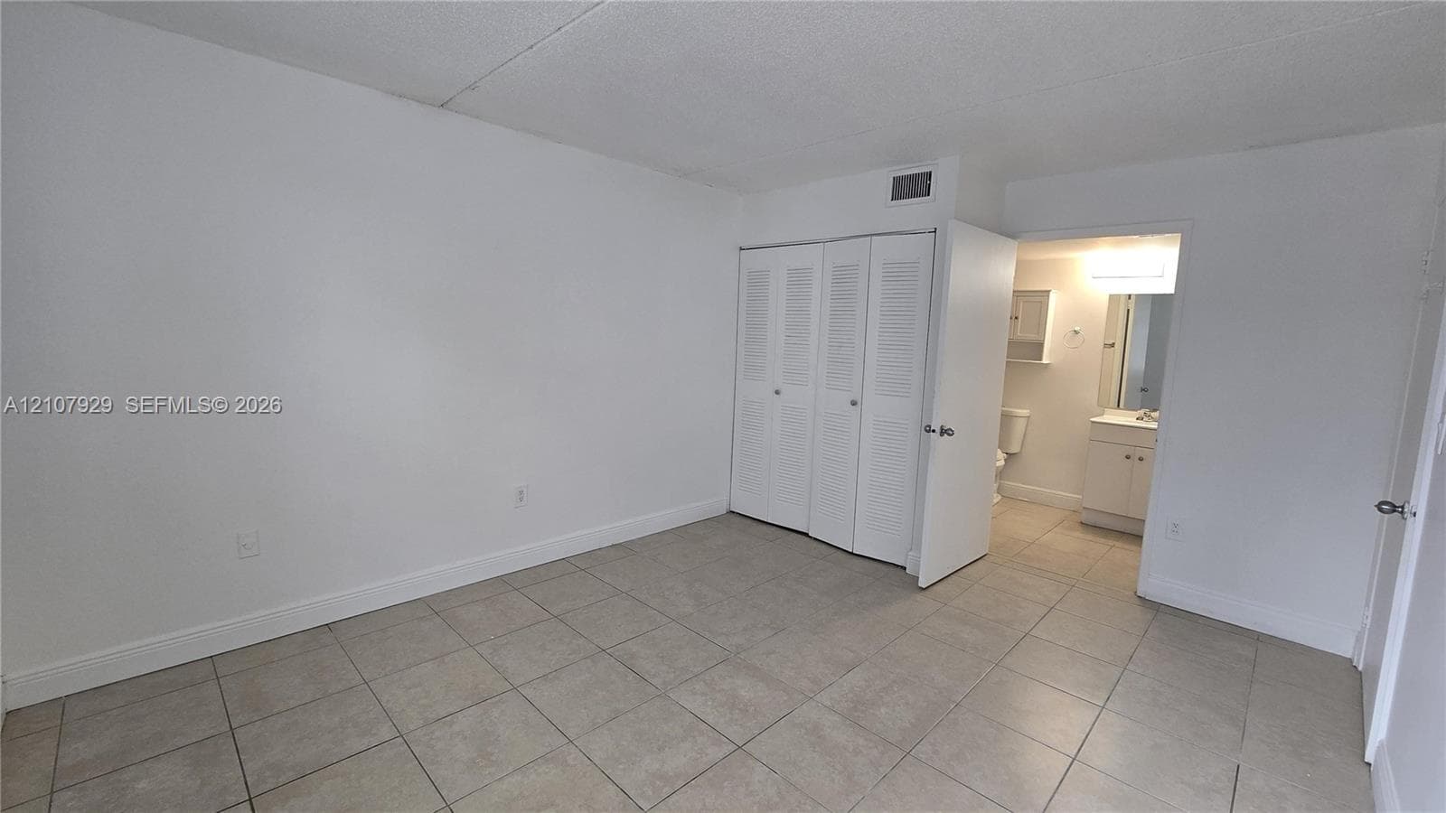 Neutral-toned ceramic tile flooring, neutral wall finishes, and built-in closet with louvered doors