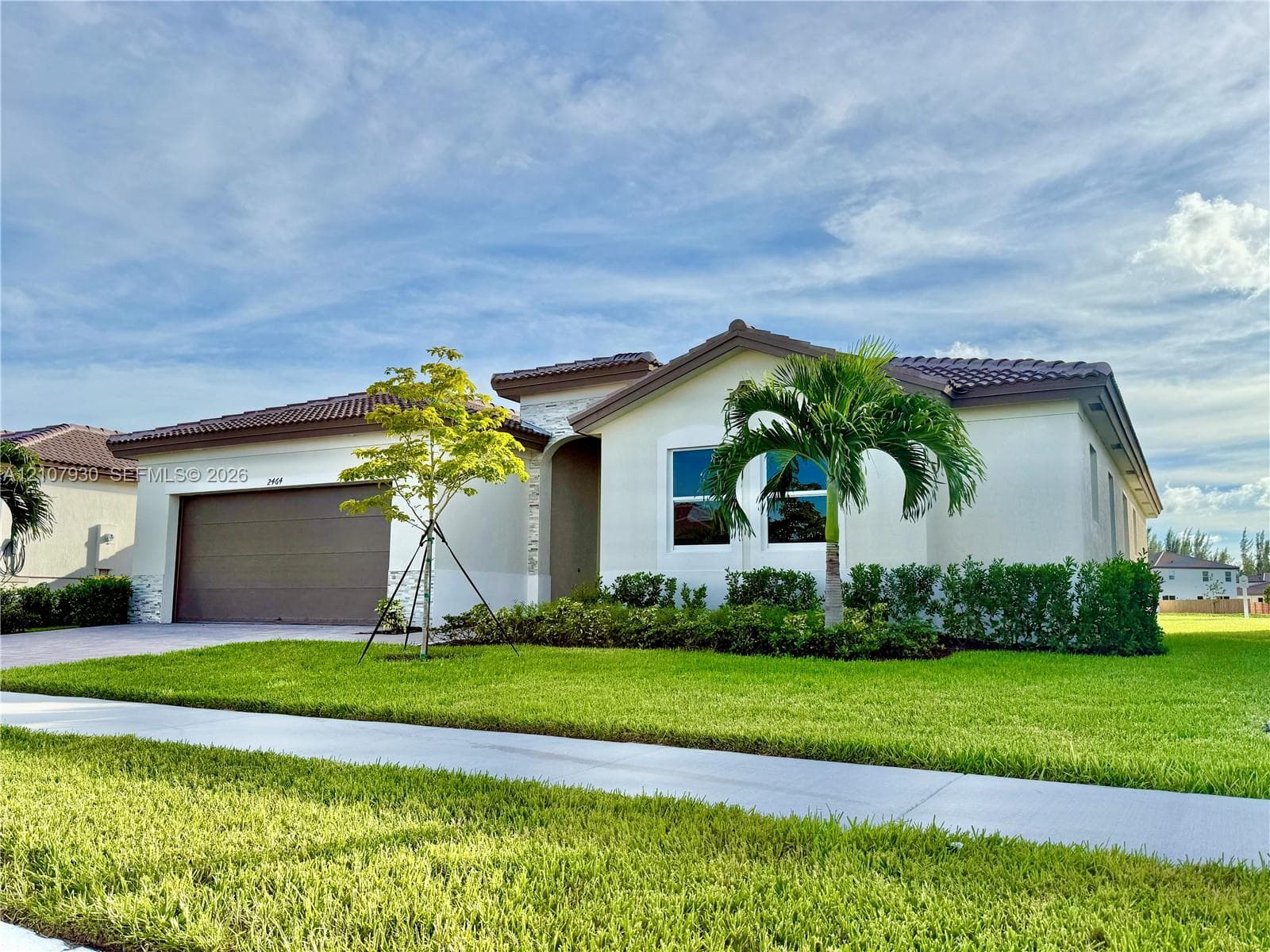 Single-story exterior featuring a tile roof, light-toned stucco facade, stone masonry accents, multi-car garage, and manicured landscaping