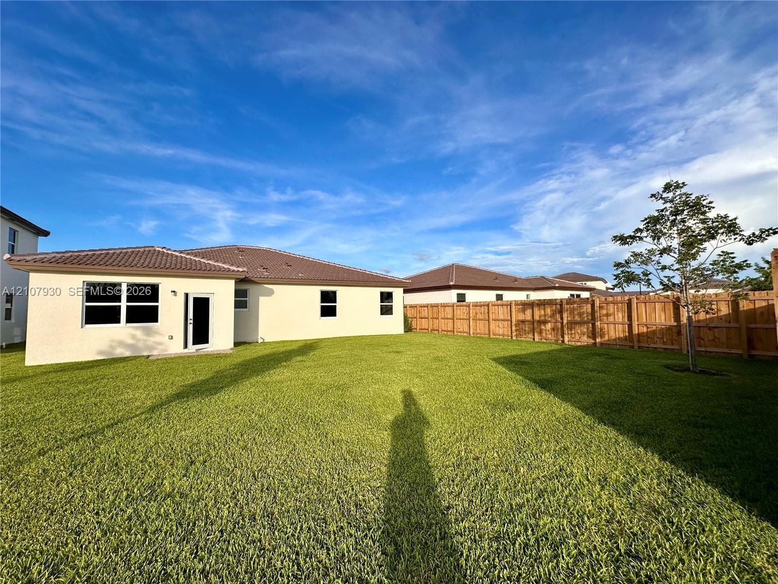 Spacious backyard featuring a grass lawn, perimeter wood fencing, and a stucco exterior with a tiled roof