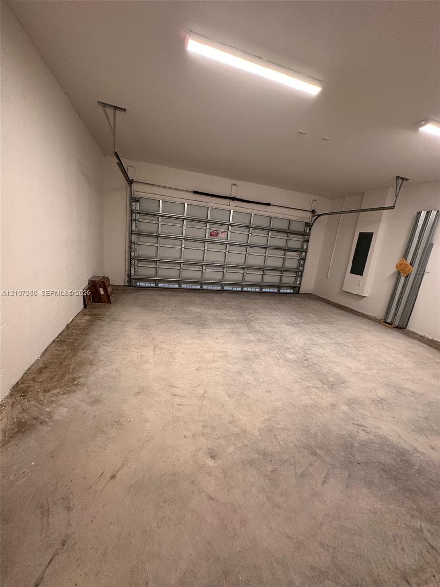 Multi-car garage featuring a sectional overhead door, finished walls, concrete flooring, and ceiling-mounted fluorescent lighting