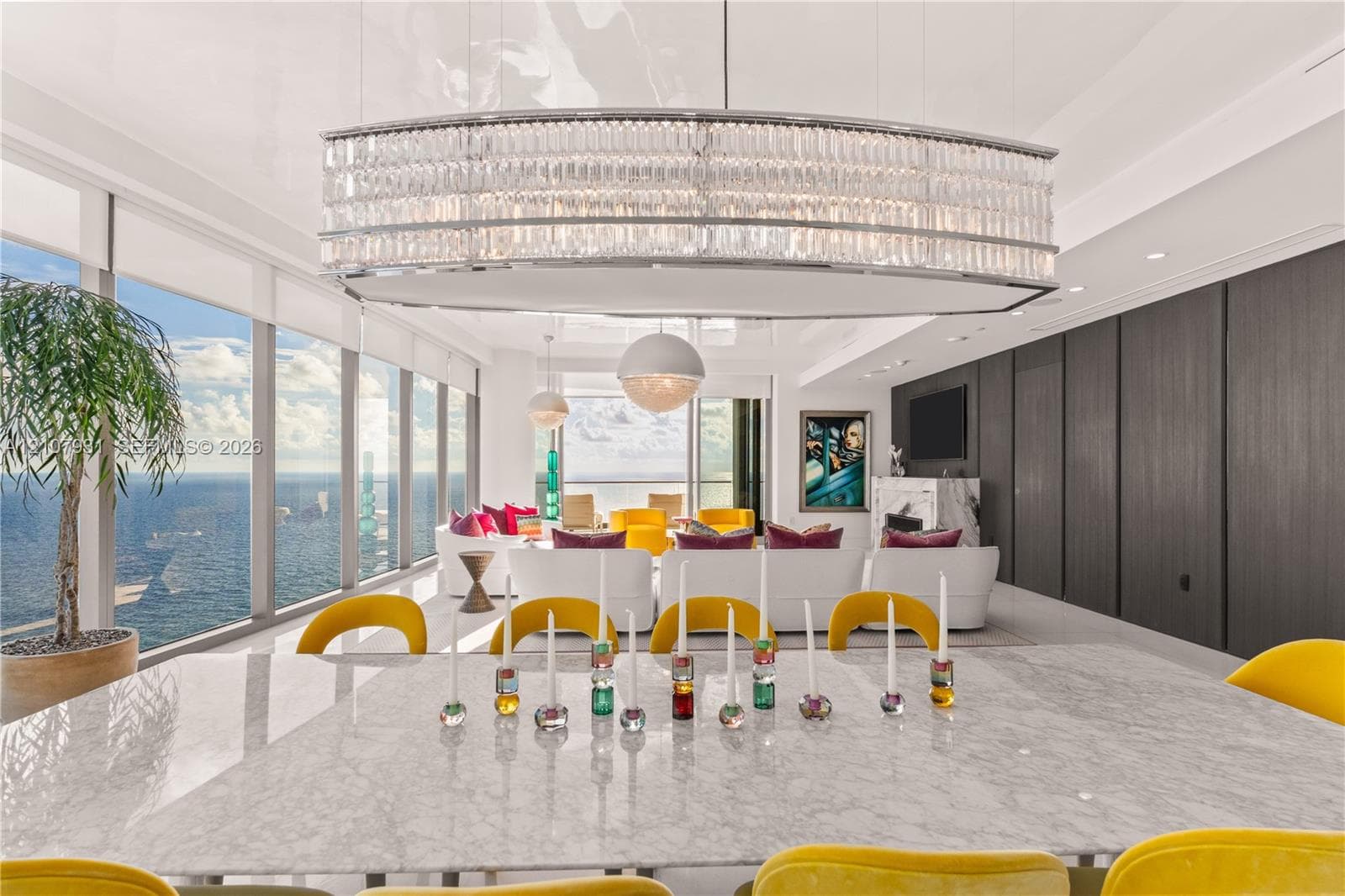 Expansive living area featuring floor-to-ceiling windows, an elongated crystal chandelier, high-gloss ceiling finish, and built-in dark wood-panel walling