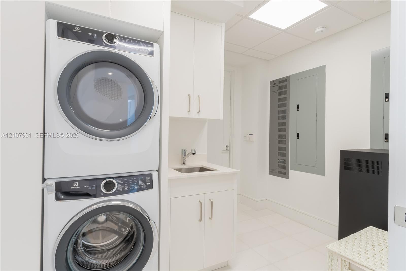 Laundry room featuring a stacked appliance set, white cabinetry, a built-in sink with a chrome faucet, and tile flooring