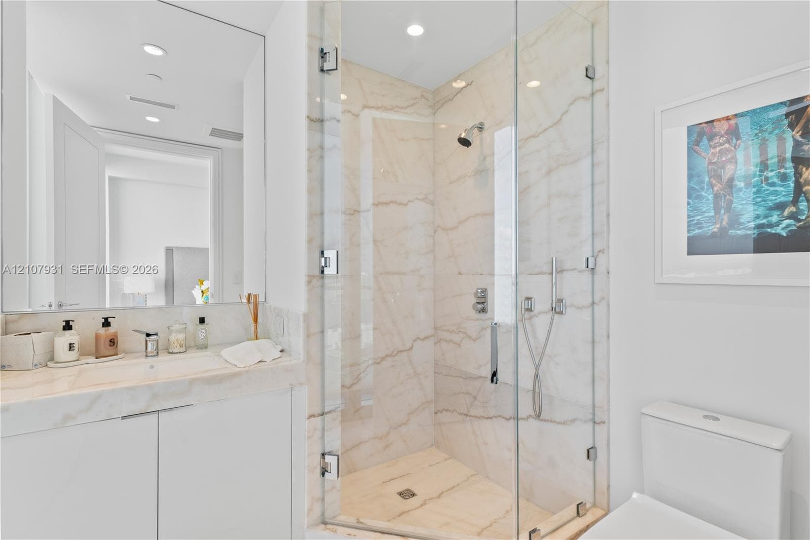 Bathroom featuring a vanity with integrated sink and stone countertop, frameless glass-enclosed shower with stone-surround, wall-to-wall mirror, and recessed lighting
