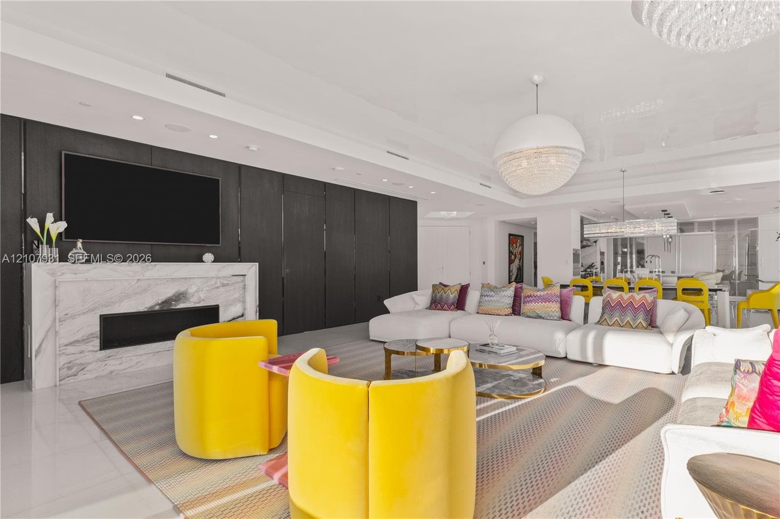 Contemporary living area featuring a stone fireplace surround, dark wood-paneled accent wall, large-format tile flooring, recessed ceiling lighting, and decorative pendant fixtures
