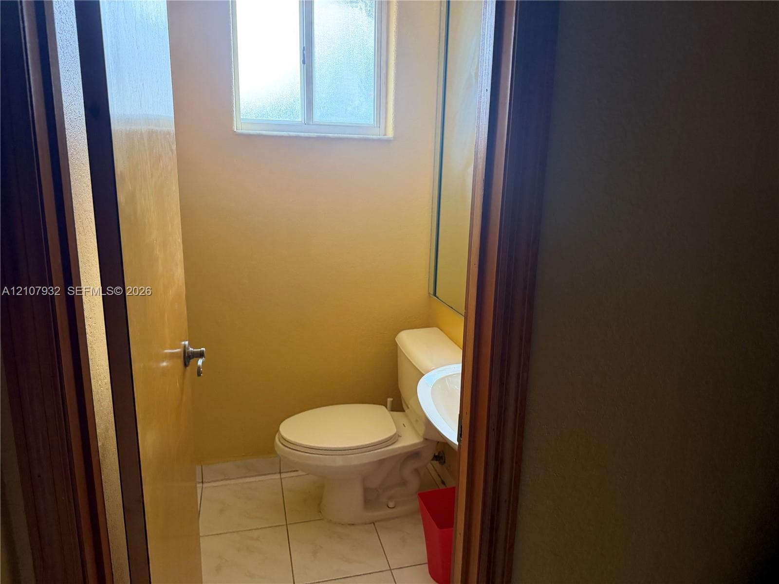 Restroom featuring tile flooring, a wall-mounted vanity with a ceramic sink, a mirror, and an obscure glass window