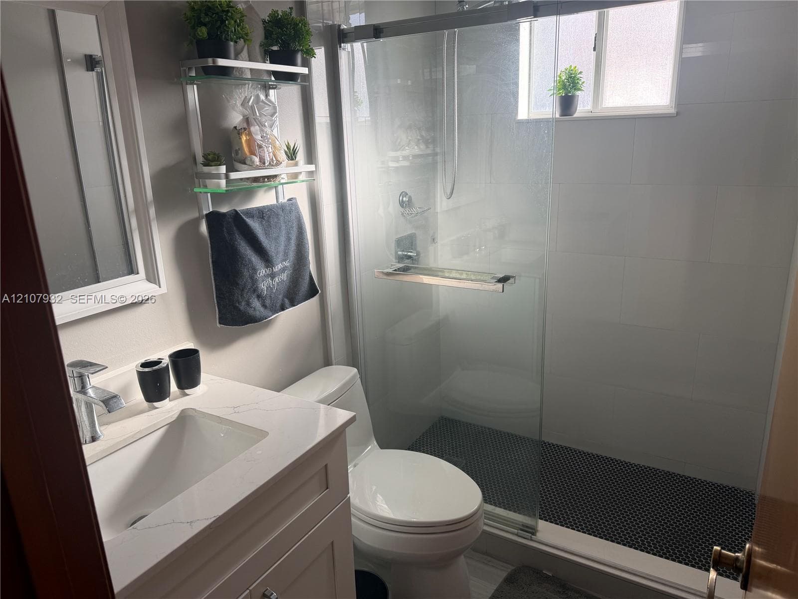 Bathroom featuring a stone-look countertop with an integrated sink, glass-enclosed shower with tiled surround, and mosaic-tiled shower flooring