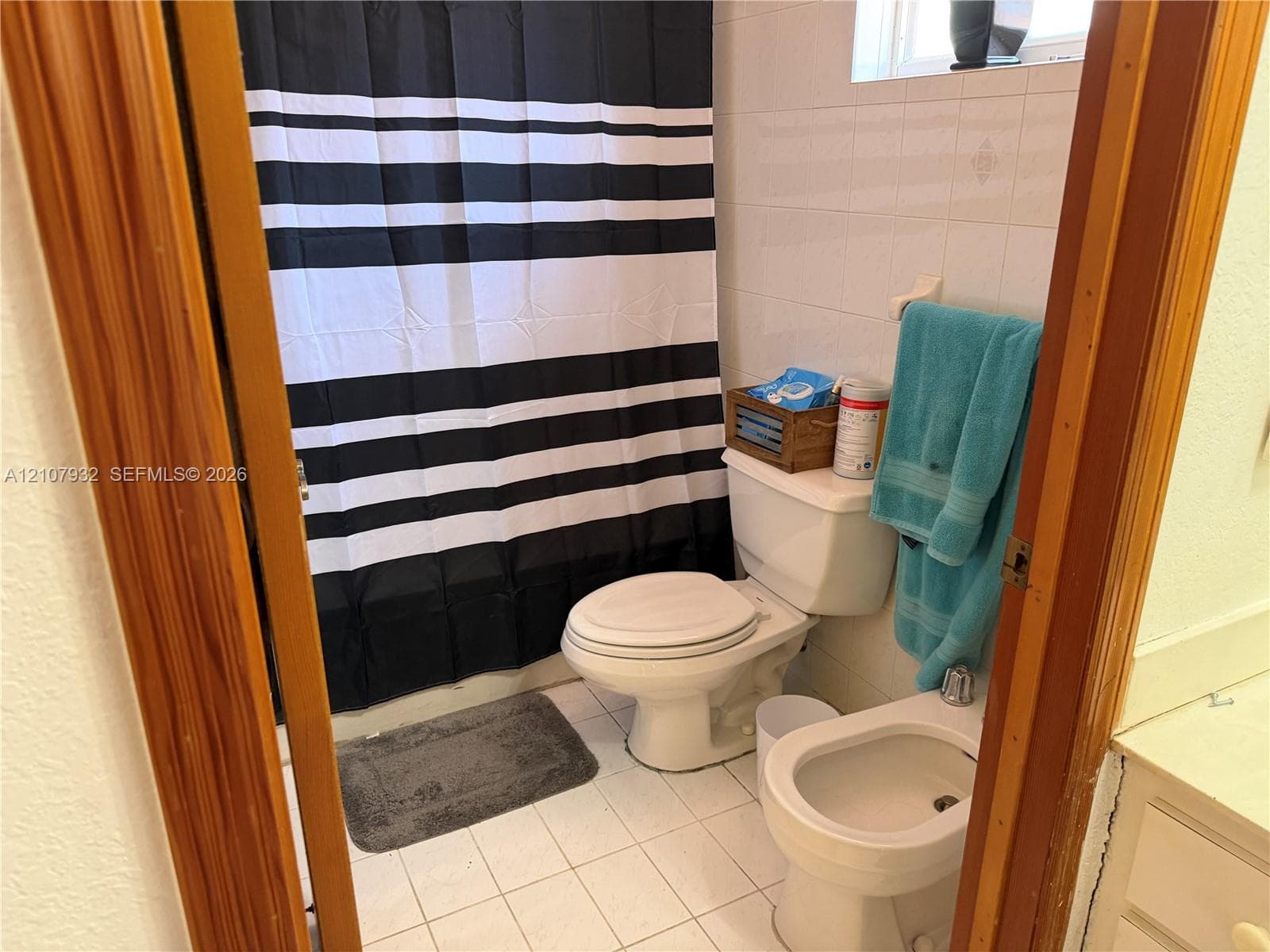 Full bathroom featuring white ceramic wall tiling, a combination tub and shower, a standard porcelain toilet, and a bidet