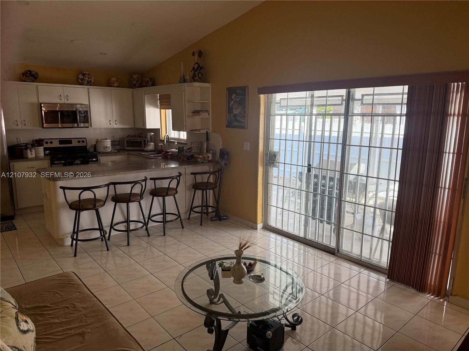 Kitchen featuring white cabinetry, stone-finish countertops, stainless steel microwave, and tile flooring, with glass sliding doors providing exterior access