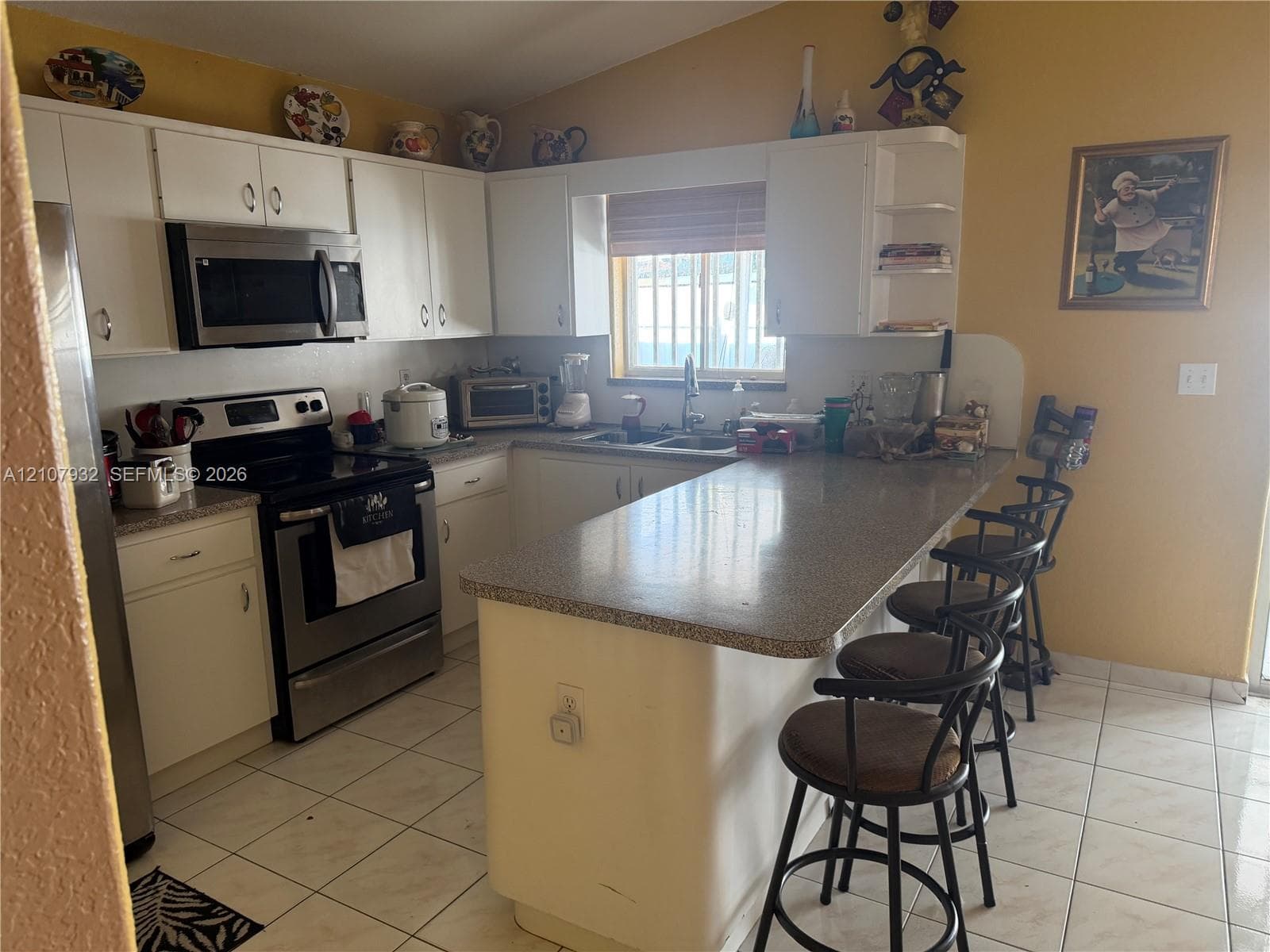 Kitchen featuring white cabinetry, stainless steel appliances, solid surface countertops, a peninsula with breakfast bar seating, and tile flooring