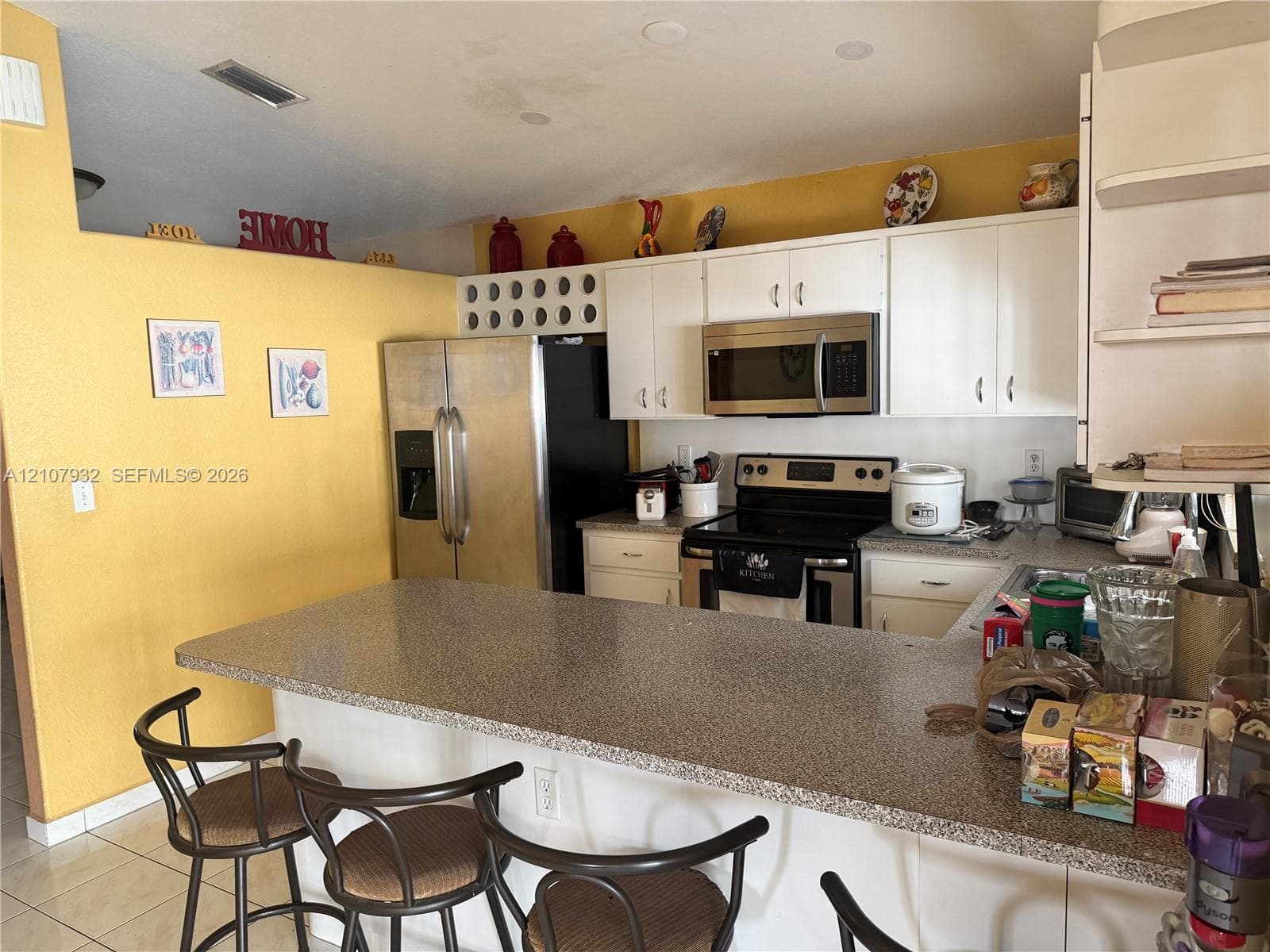 Kitchen featuring a wrap-around stone-finish countertop, white cabinetry with integrated wine storage, stainless steel refrigerator, and built-in microwave