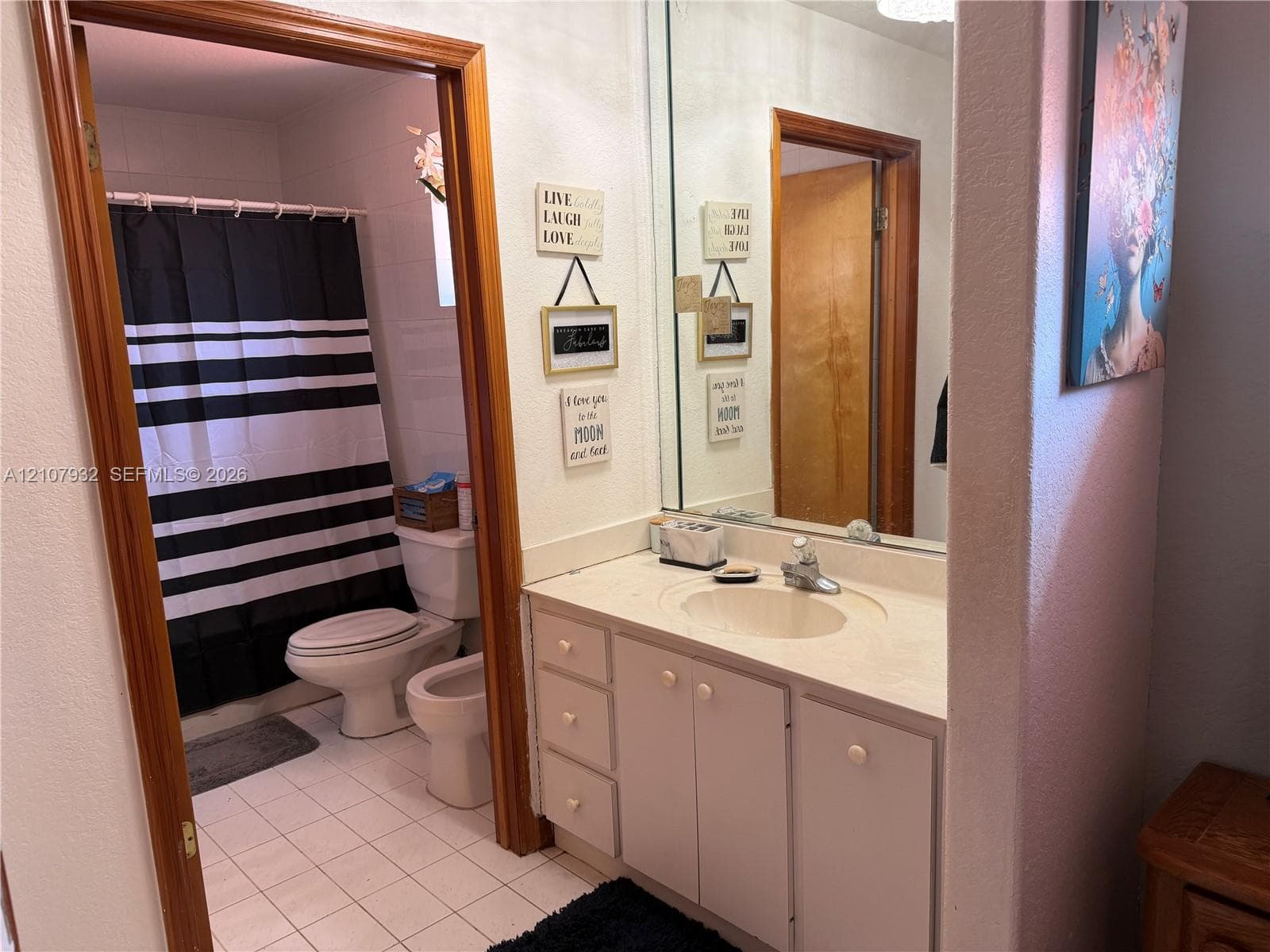 Bathroom featuring a vanity with integrated sink and countertop, large wall-mounted mirror, white cabinetry, and ceramic tile flooring