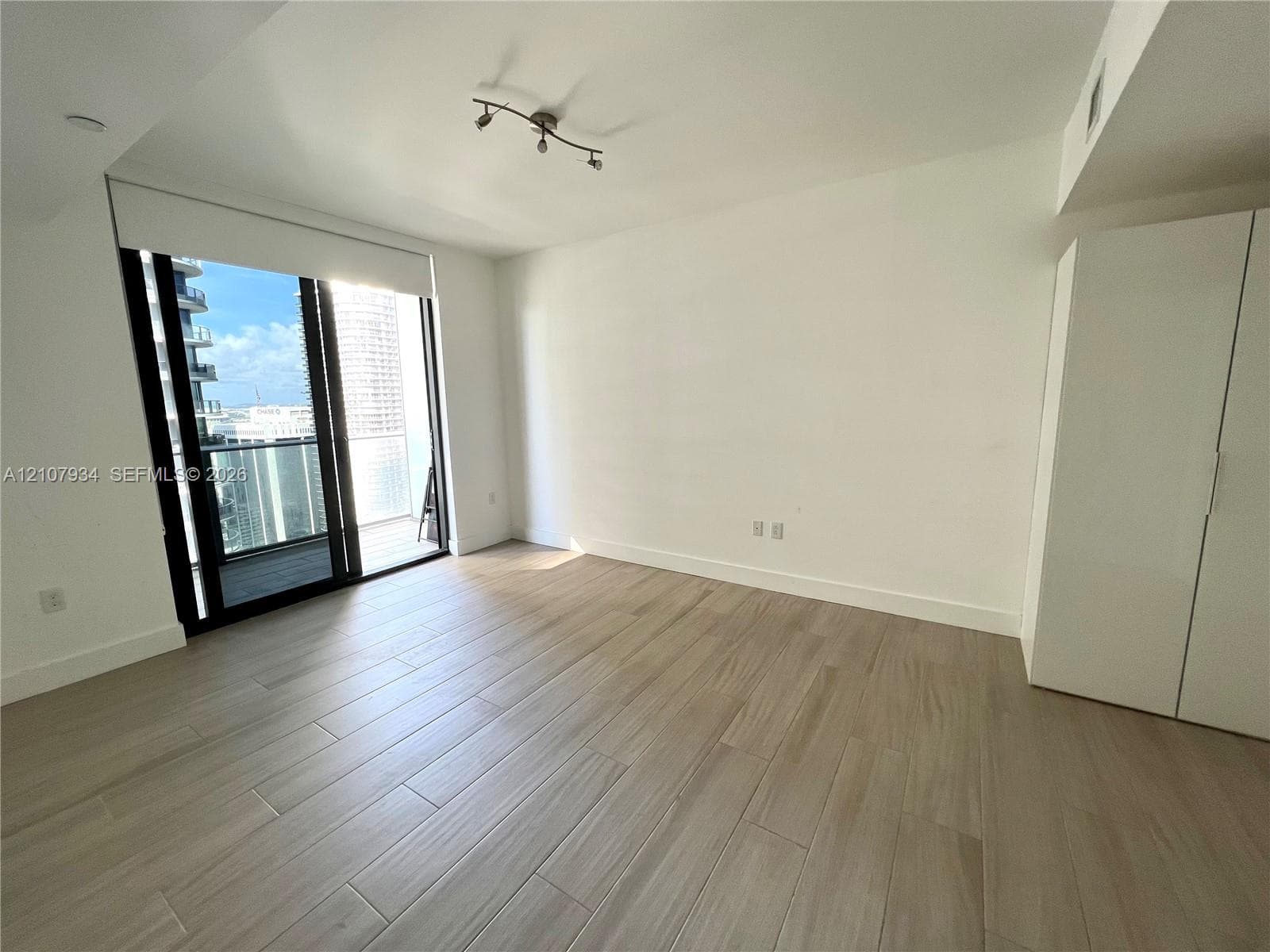 Neutral-toned wood-finish flooring, floor-to-ceiling glass sliding door, private balcony, built-in floor-to-ceiling cabinetry, and modern track lighting