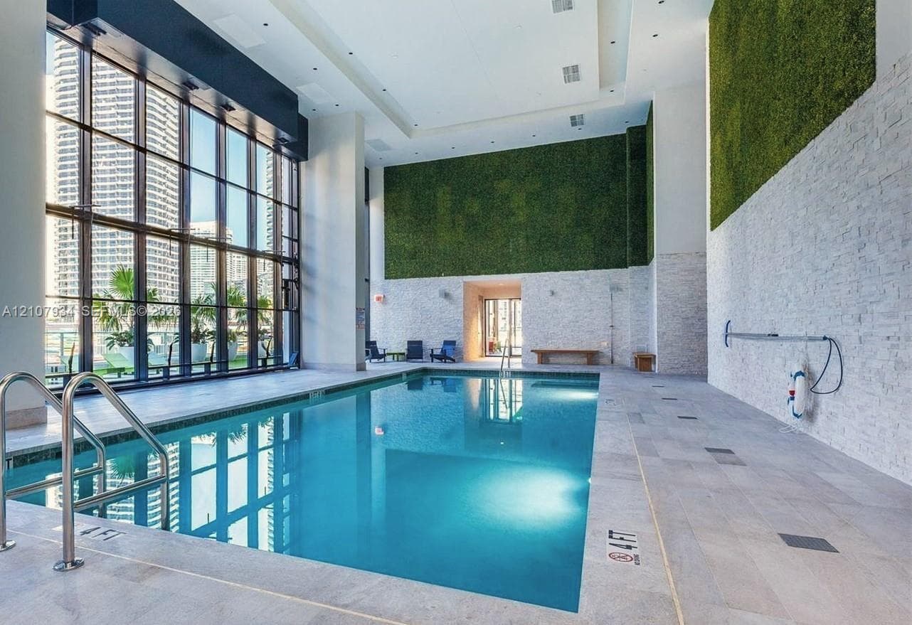 Indoor swimming pool featuring floor-to-ceiling windows, stacked stone accent walls, integrated vertical garden installations, and large-format tile decking