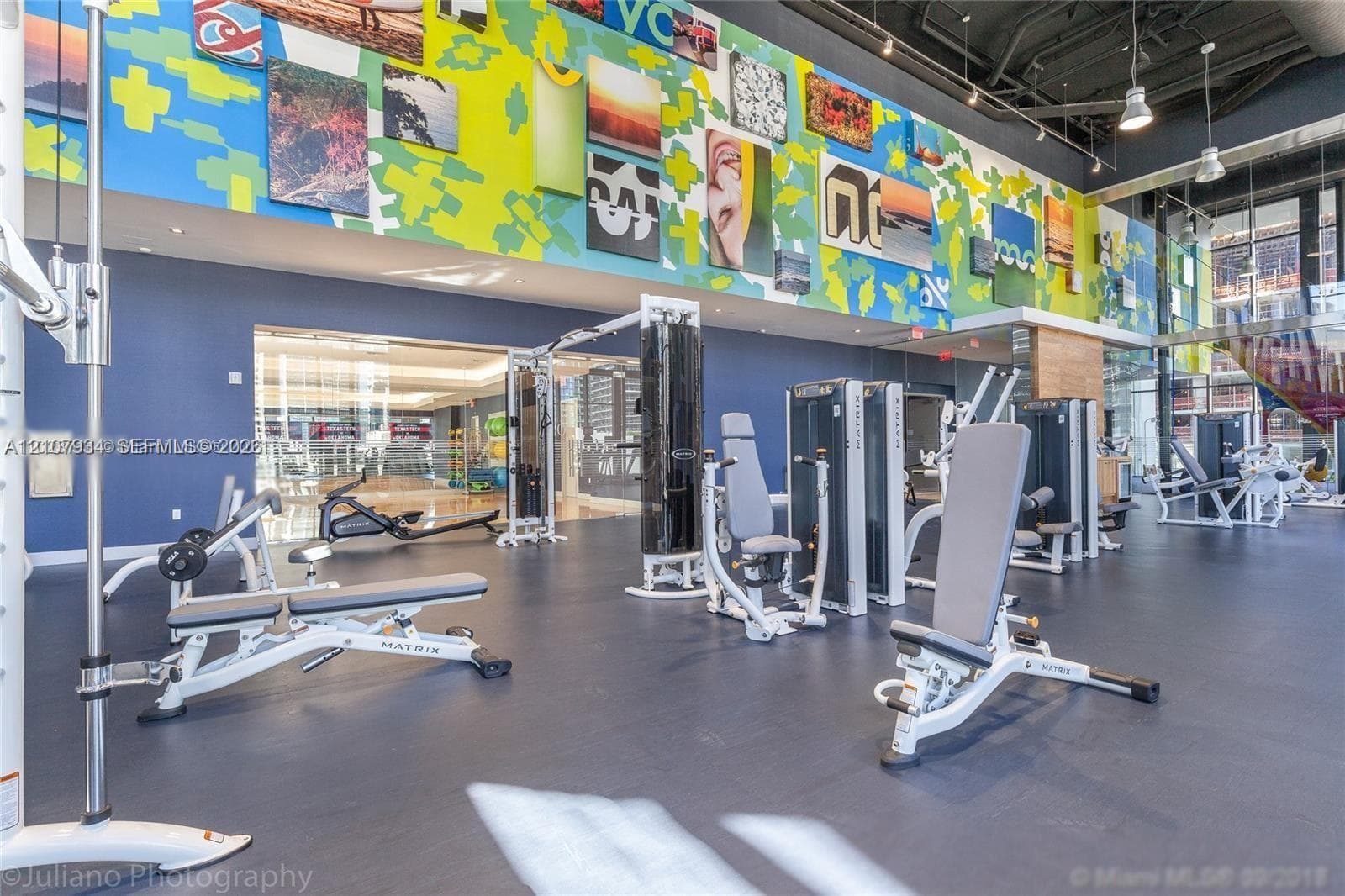 Fitness center featuring high ceilings with exposed mechanicals, rubber flooring, floor-to-ceiling windows, and wall-mounted art installation