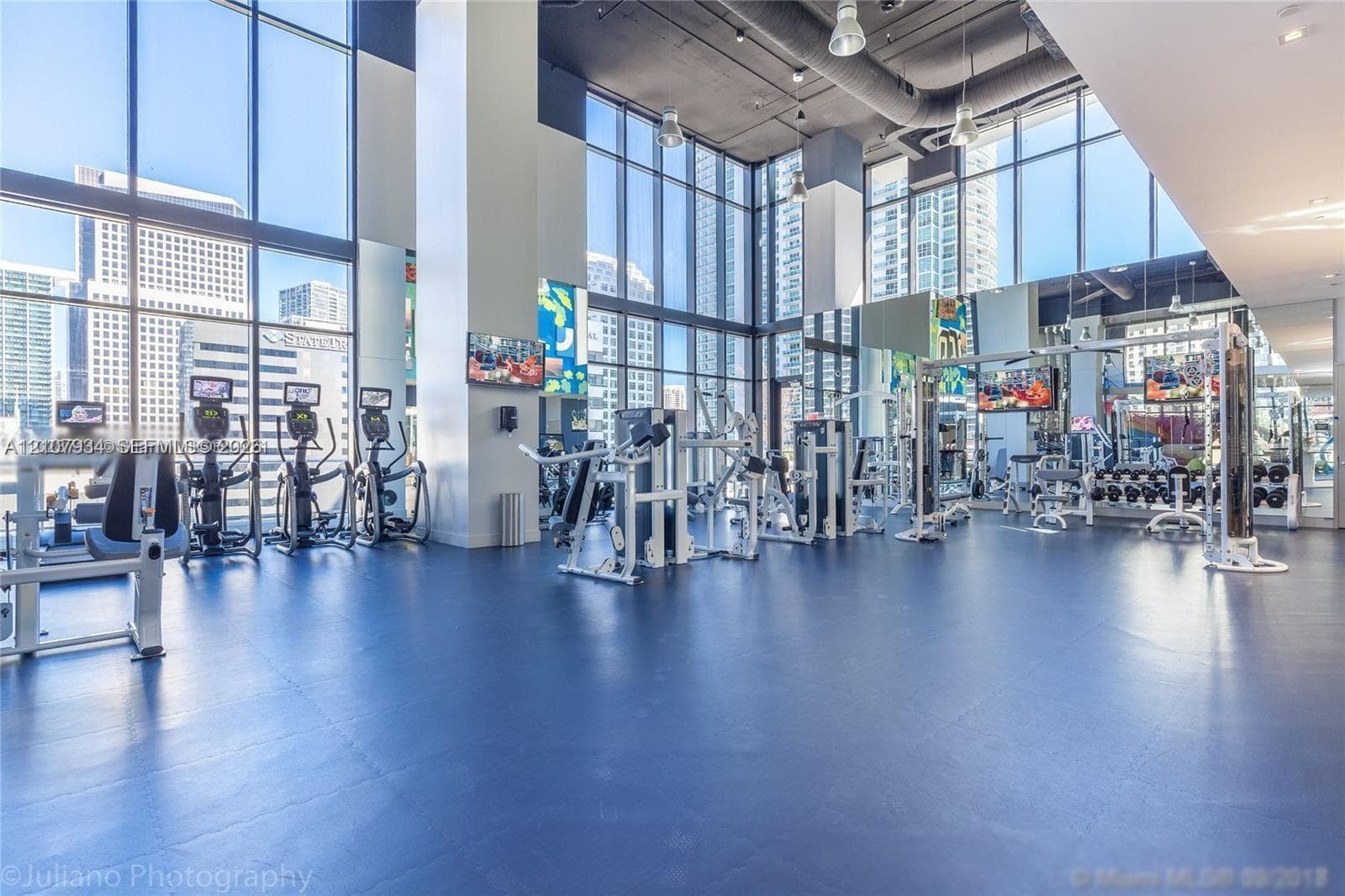 Fitness center featuring floor-to-ceiling windows, high ceilings with exposed mechanical elements, mirrored walls, and rubberized athletic flooring