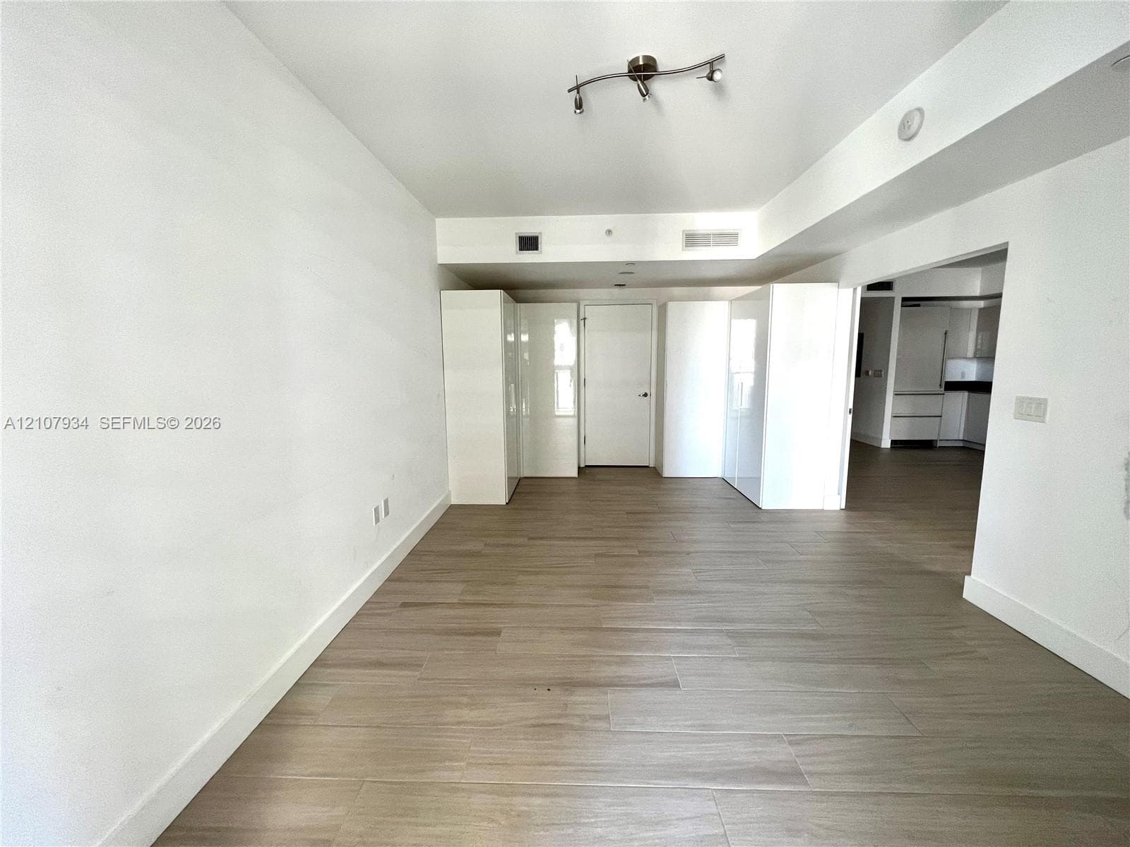 Open-concept interior featuring light wood-finish flooring, built-in white cabinetry, and multi-directional track lighting